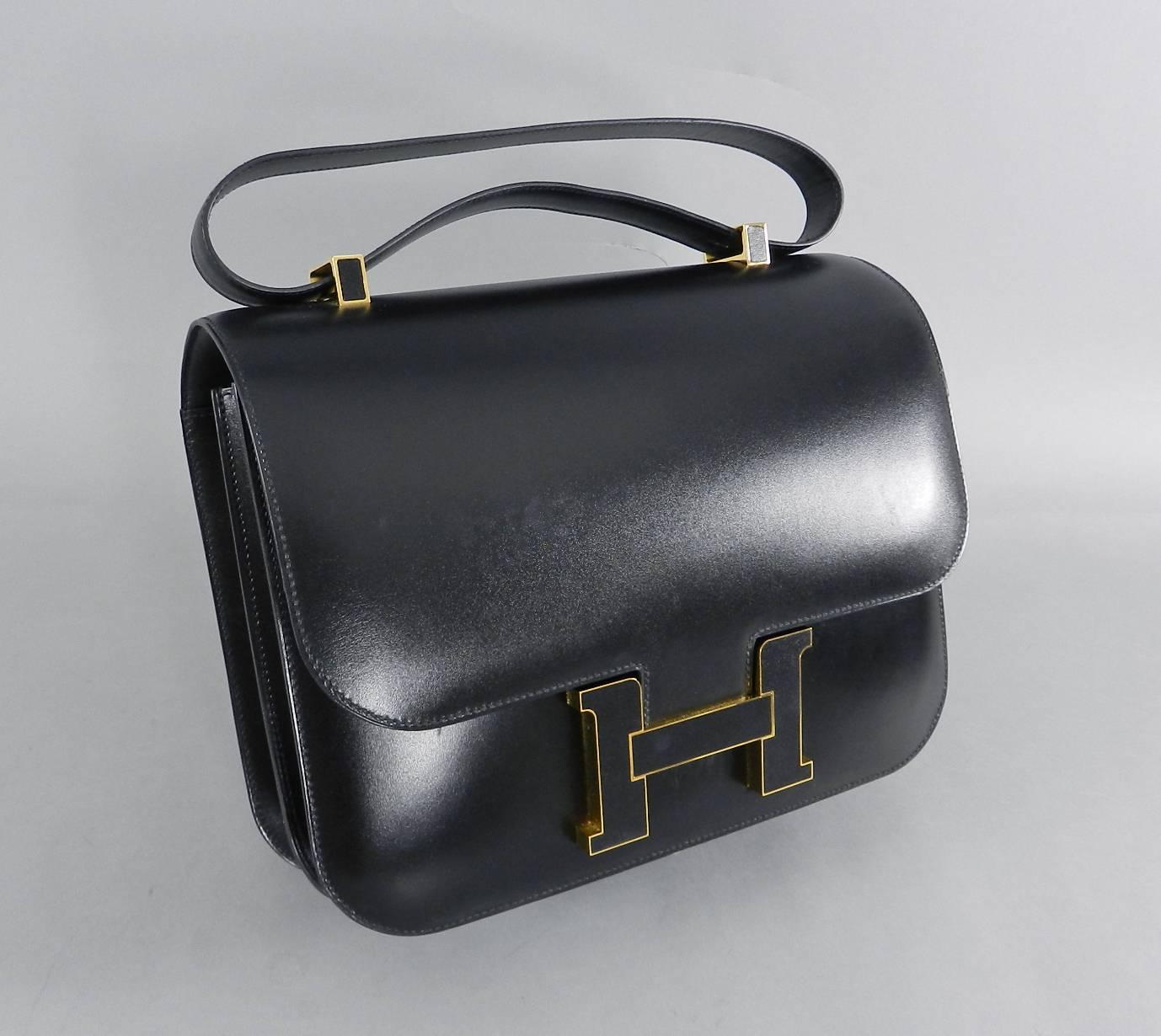Hermes Limited Edition Constance Cartable Black Box Leather with Gold Hardware.  29cm. The bag features a uniquely constructed looping top handle strap with goldtone hardware links. The top flap tucks into a prominent H in goldtone hardware with