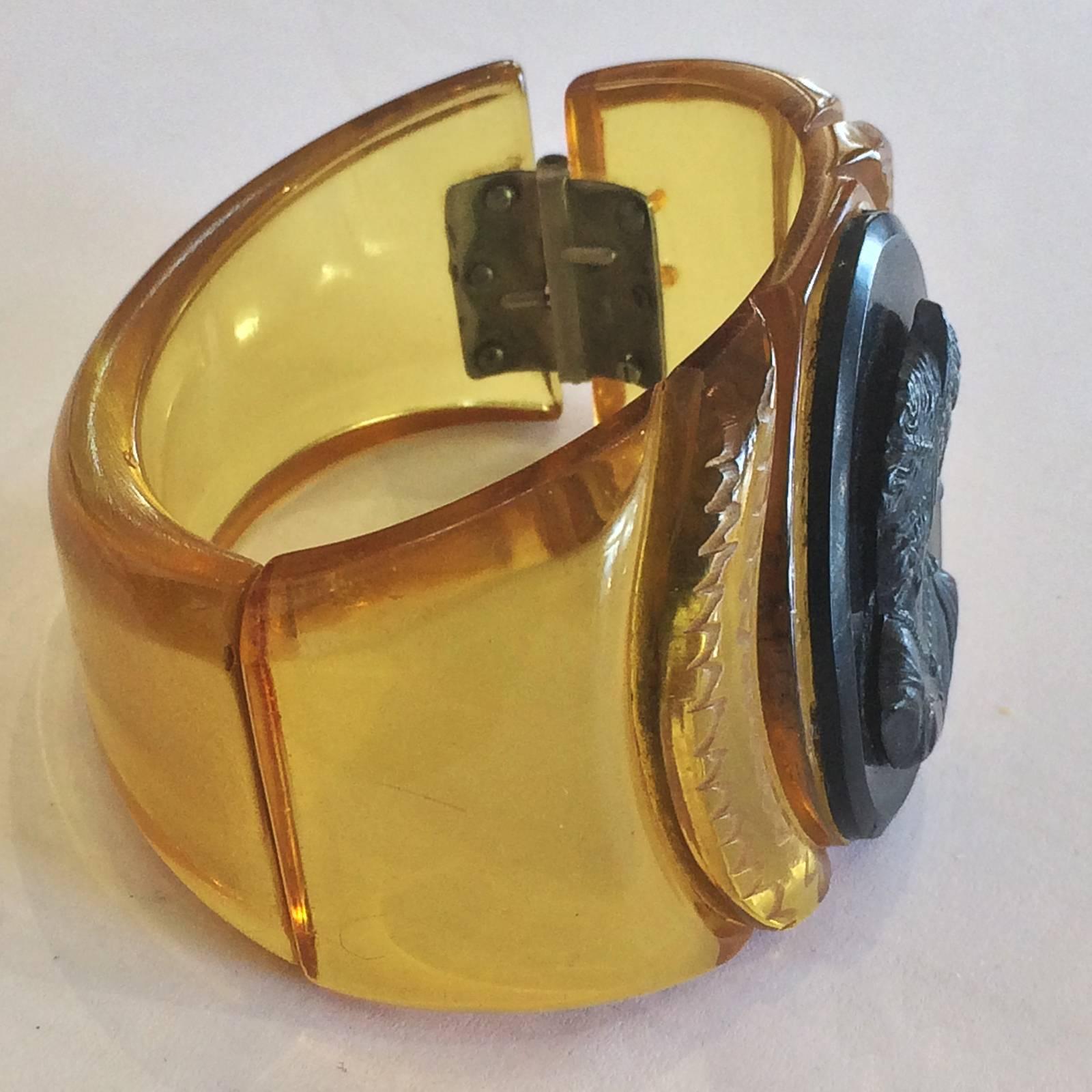 Art Deco Clamper Bangle in carved Apple juice Bakelite, set with a lozenge of black Bakelite, with a carved  Bakelite Cameo. No damage, losses or repairs. The original spring hinge works perfectly with no distortion. An excellent example of serious