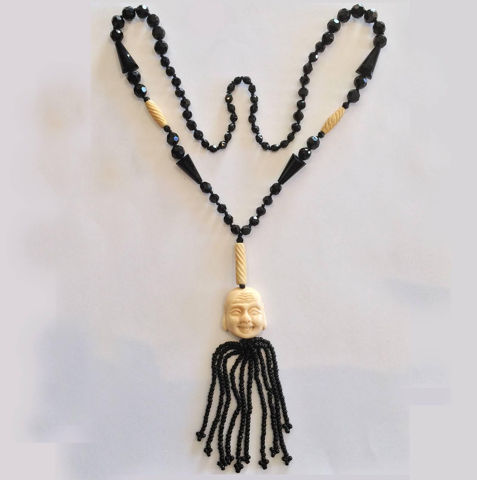 Art Deco Necklace in French Jet and Carved bone. Smiling Buddha Face and Carved “twists”, both in Bone The remainder of the Necklace is in French Jet, with Tapered Jet beads, all faceted with also tapered “pyramids” and Jet Tassel in microbeads,