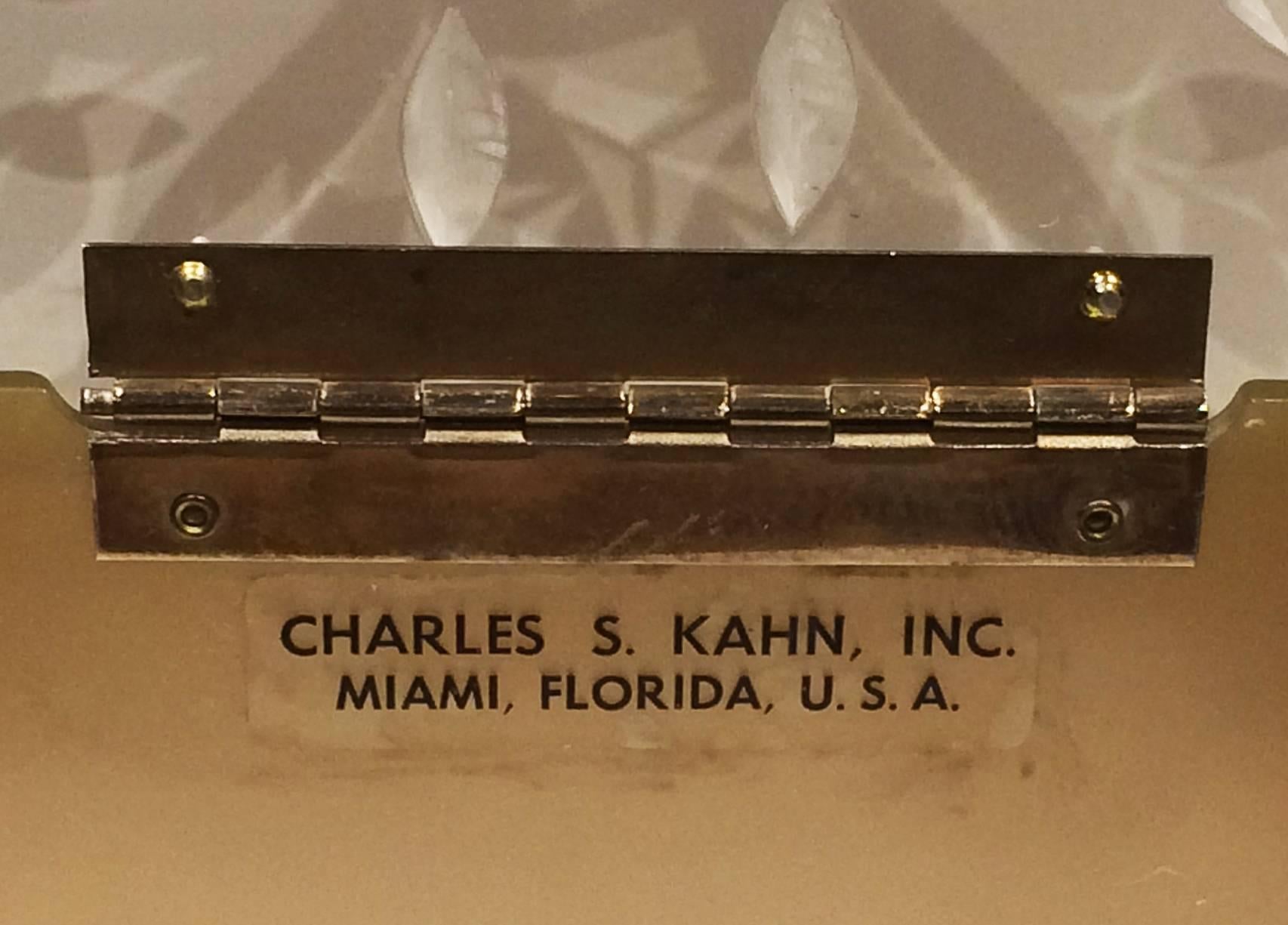 1950s lucite purse or handbag with soft gold sides, clear base, top and handle in clear with satin carved central Daisy and Leaf trims. Internally Labelled “CHARLES S. KAHN, INC.” above “MIAMI FLORIDA U. S. A. “. All metalwork, Piano Hinge, Handle