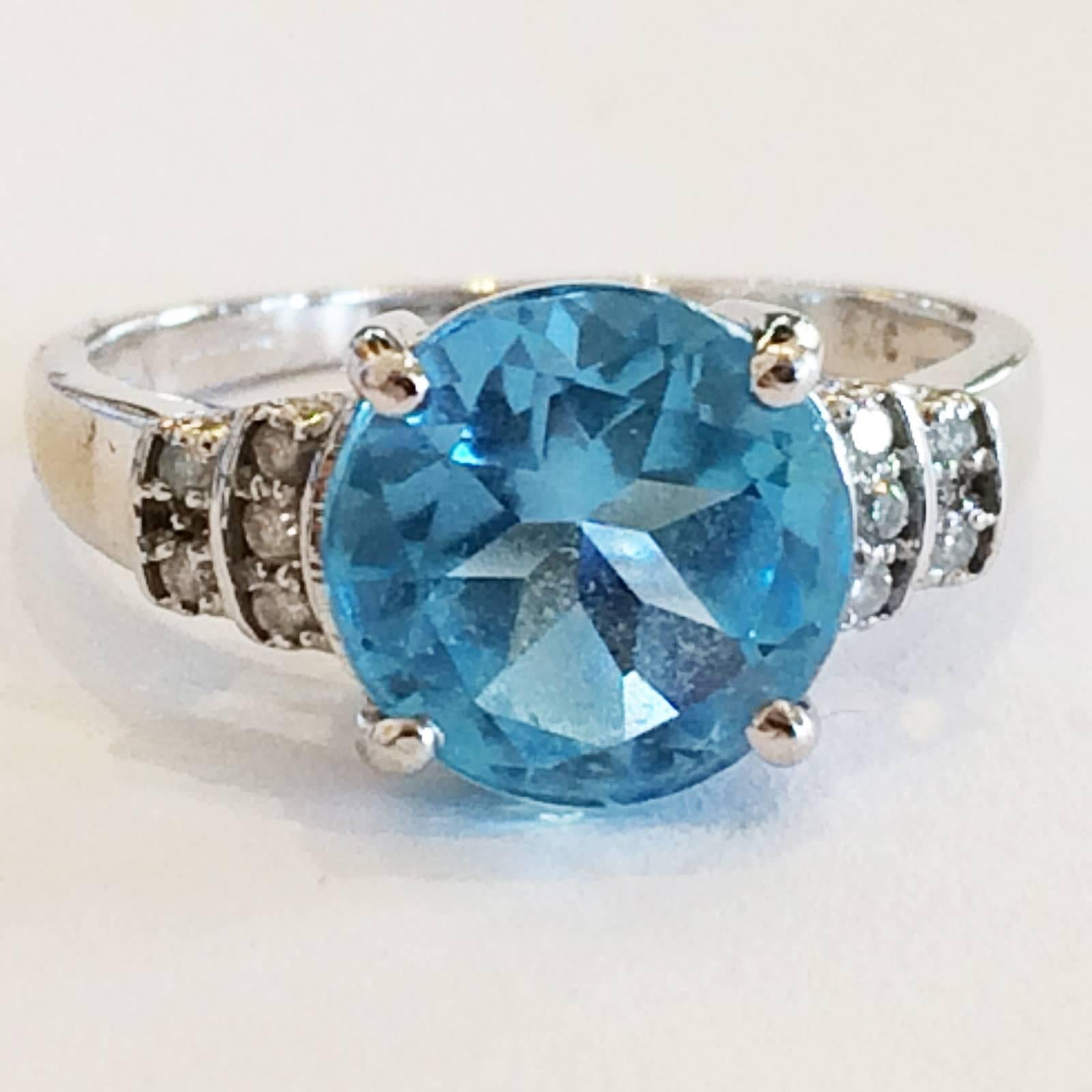 Mid Century Ring of 9Kt White Gold, with a large, Brilliant Blue Topaz Gem, featured with 5 small Diamonds to each stepped shoulder. Intricately facetted Topaz, high mounted to get light in from below to show the colour even more sparkle. Full