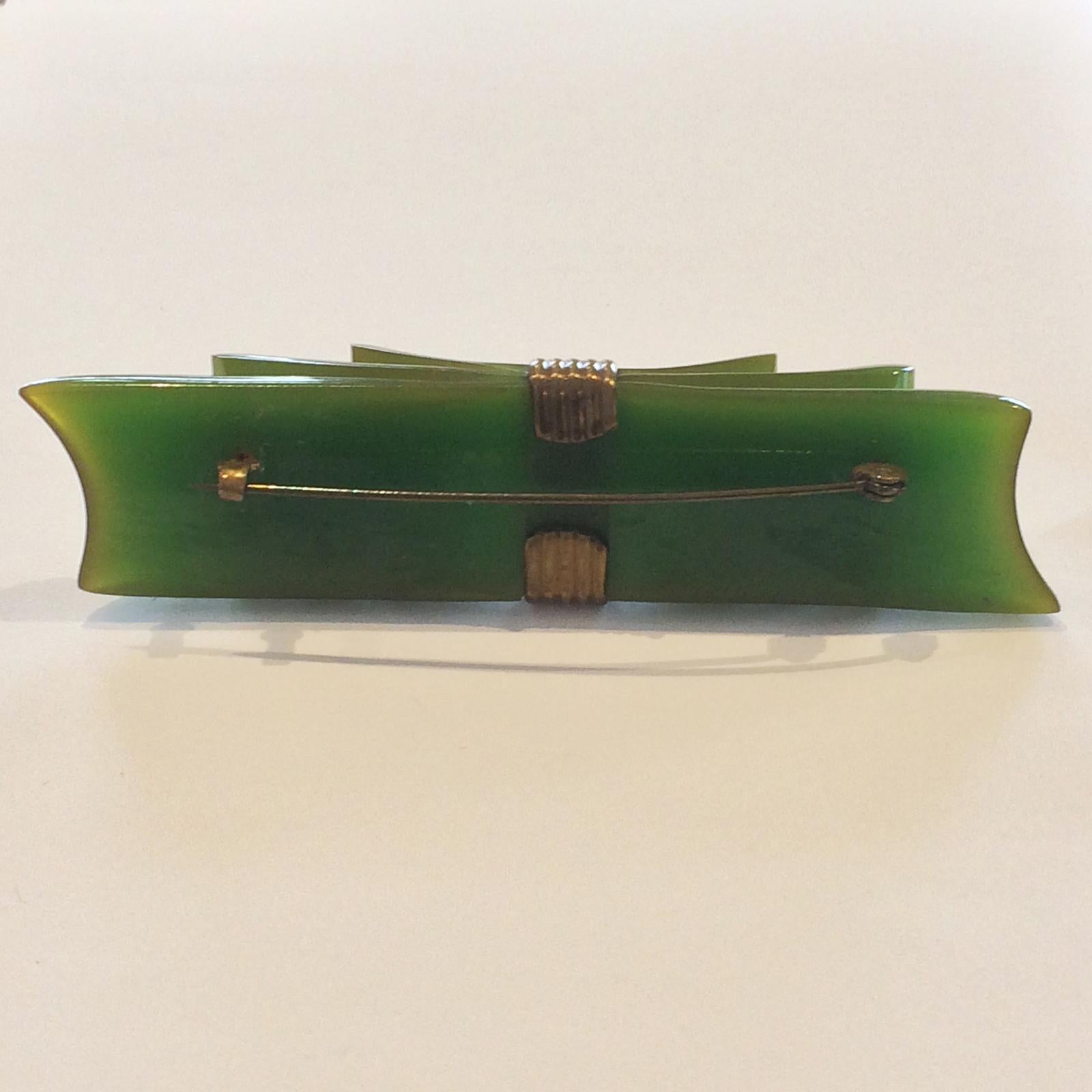 Art Deco Green Bakelite Ribbon Brooch, with bronze “tie” and Clip to rear, all in perfect, original condition. The Bakelite has a slight, and fine image of a yellow influence to the colour. All the metal items are attached in the traditional screw