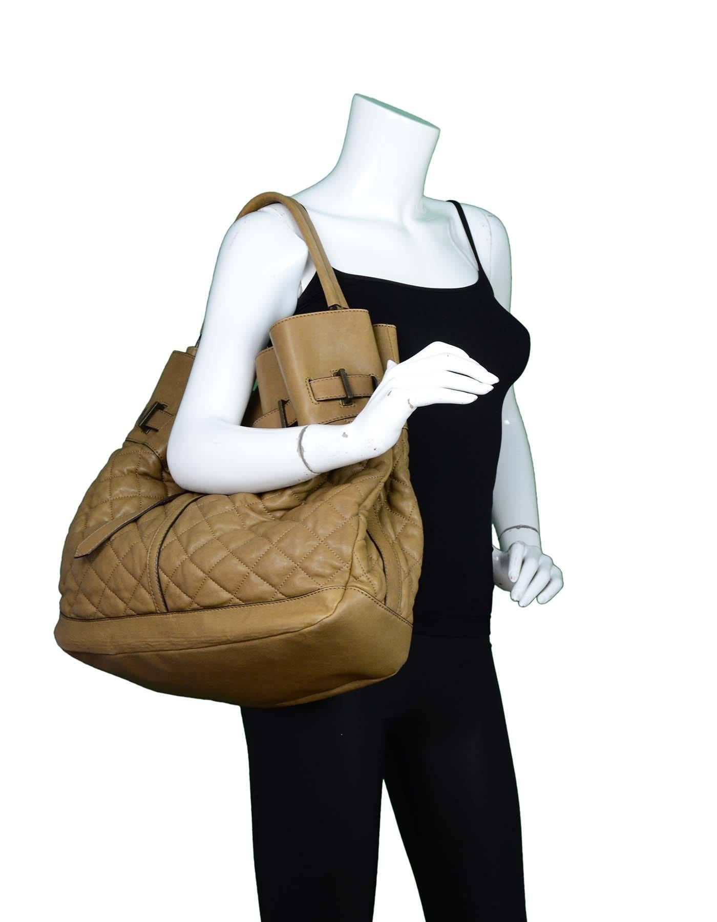 Burberry Brown Quilted Leather Tote
Features belt detail

Color: Brown
Hardware: Brass
Materials: Leather, metal
Lining: Nova check textile
Closure/Opening: Open top with center double snap
Exterior Pockets: None
Interior Pockets: Center