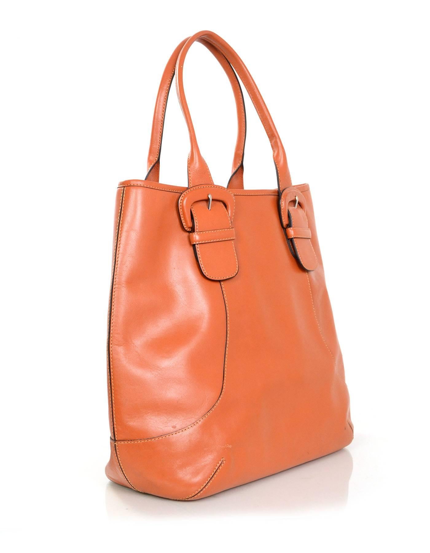 Cole Haan Orange Leather Tote 
Features oversized leather buckles at at straps

Made In: China
Color: Burnt orange
Hardware: Silvertone
Materials: Leather
Lining: Blue nylon-blend textile
Closure/Opening: Open top
Exterior Pockets: