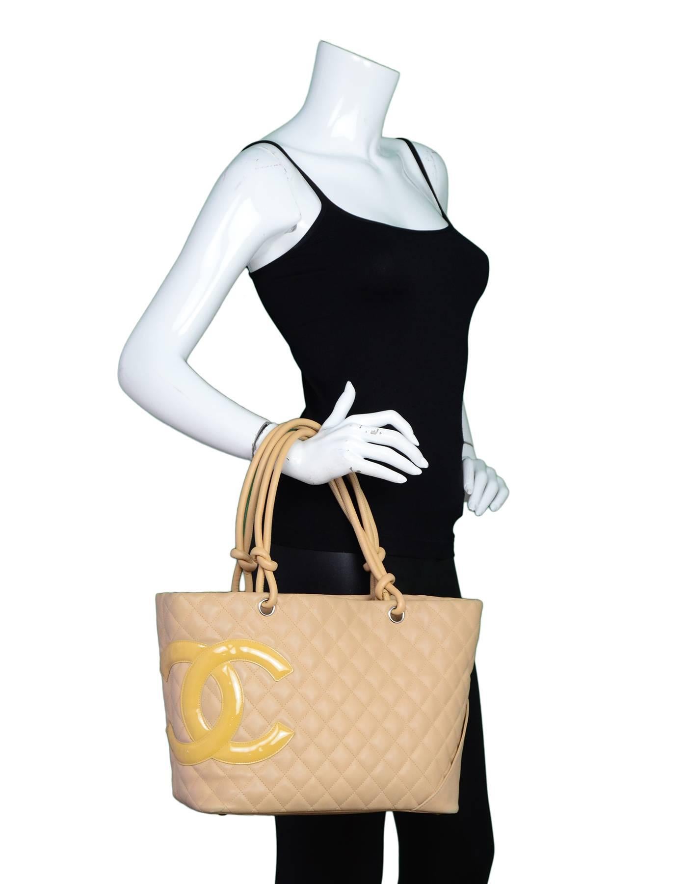 100% Authentic Chanel Beige Quilted Cambon Tote. Features oversized yellow patent leather CC logo with silvertone hardware, one back pocket and knotted shoulder straps. Interior features a vibrant orange lining with two zippered pockets and one cell
