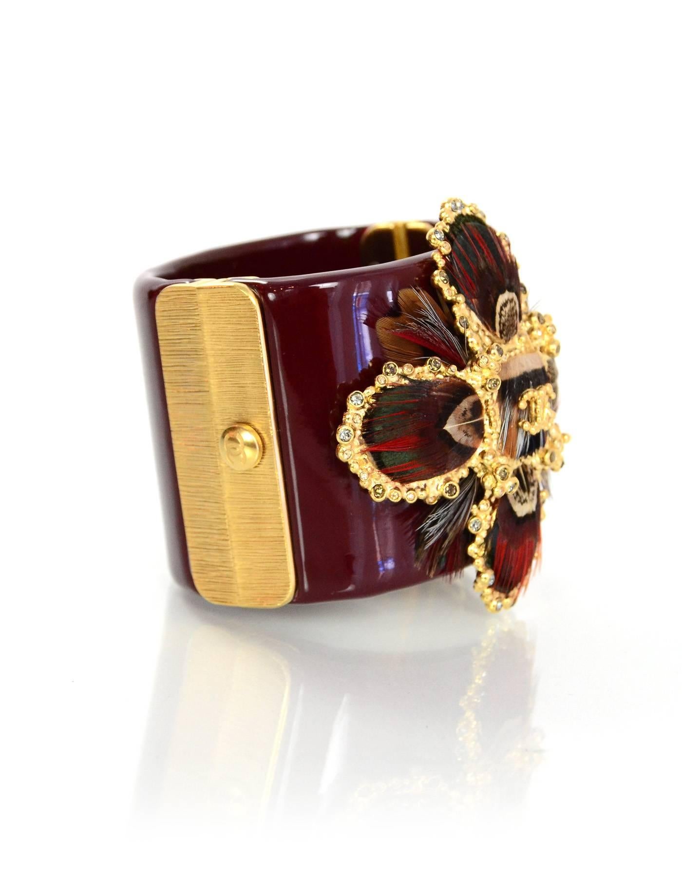 Chanel Burgundy Resin Detailed Cross Cuff 
Features goldtone metal, feather and crystal cross detail

Made In: Italy
Year of Production: 2013
Color: Burgundy and goldtone
Materials: Resin, metal, crystal, and feather
Closure: Push clasp