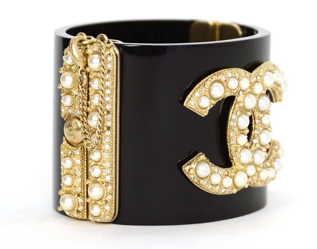 Chanel Black Resin Clamper Cuff w/Pearl & Crystal CC
Features faux pearl and crystal CC and detailing set in light goldtone metal

    Made in: France
    Year of Production: 2014
    Stamp: 14 CC C
    Closure: Push lock clamper with securing
