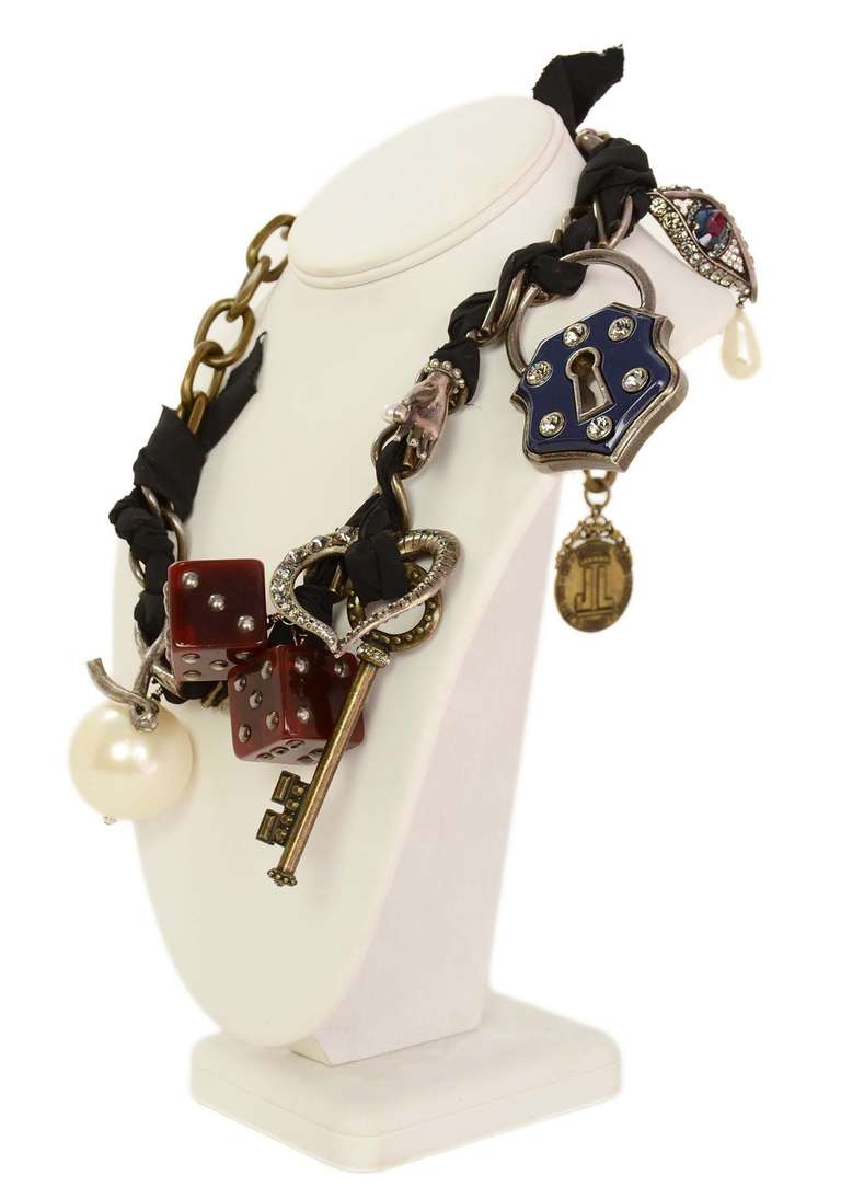 Antiqued brass tone chain intertwined with black silk.
Oversized charms include the following: 
Large faux pearl 
Two tortoise resin dice
A brass key with Swarovski crystals 
A brass heart with Swarovski crystals 
A brass lock with navy resin