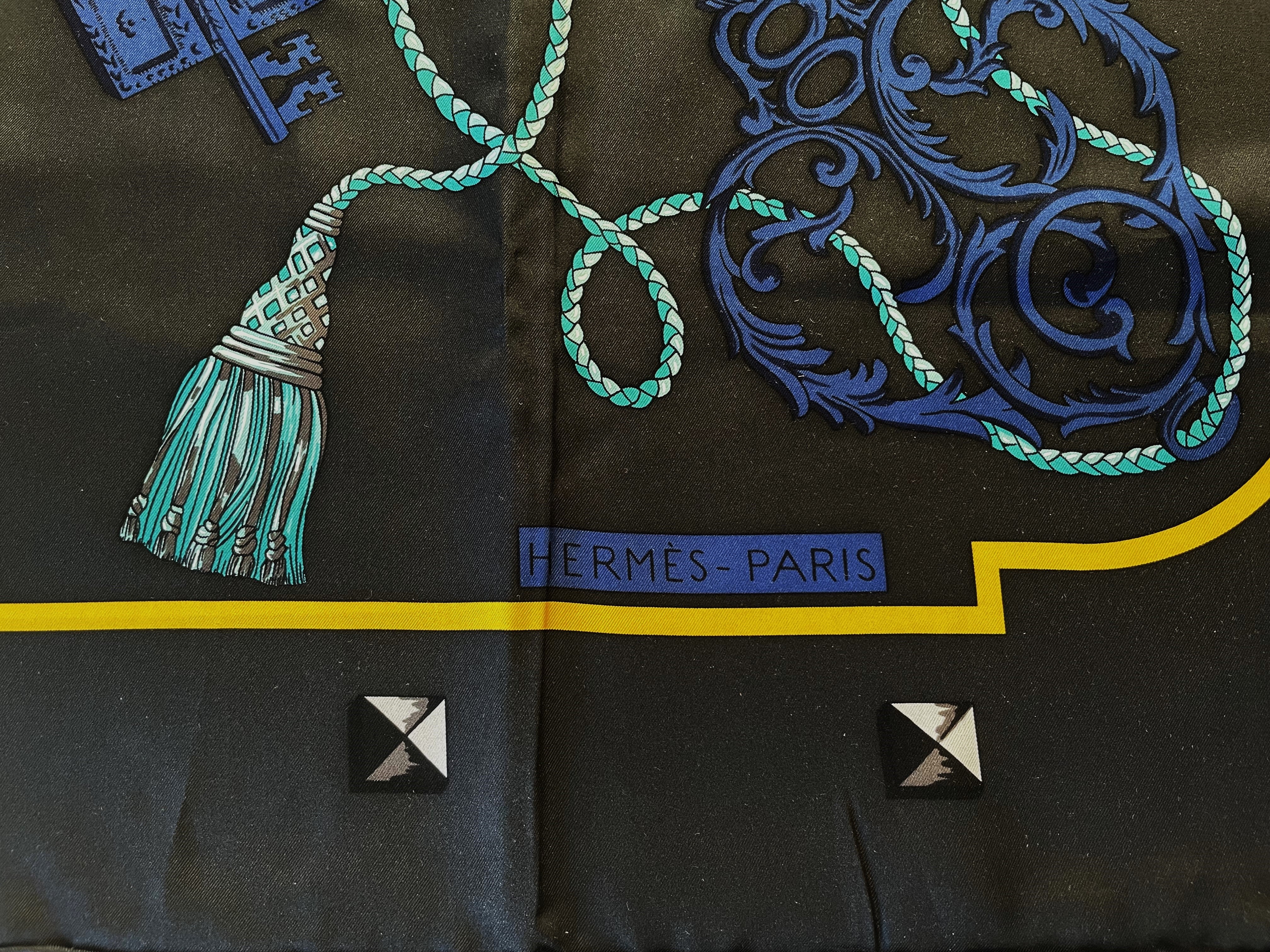 Hermes large 100 % silk scarf, 140 x 140 cm larg,  with blue and gray keys motives , hand-rolled by HERMÈS with a key motif on an anthracite-colored background. Turquoise colored cord with tassel runs through the whole cloth. A yellow stripe frames