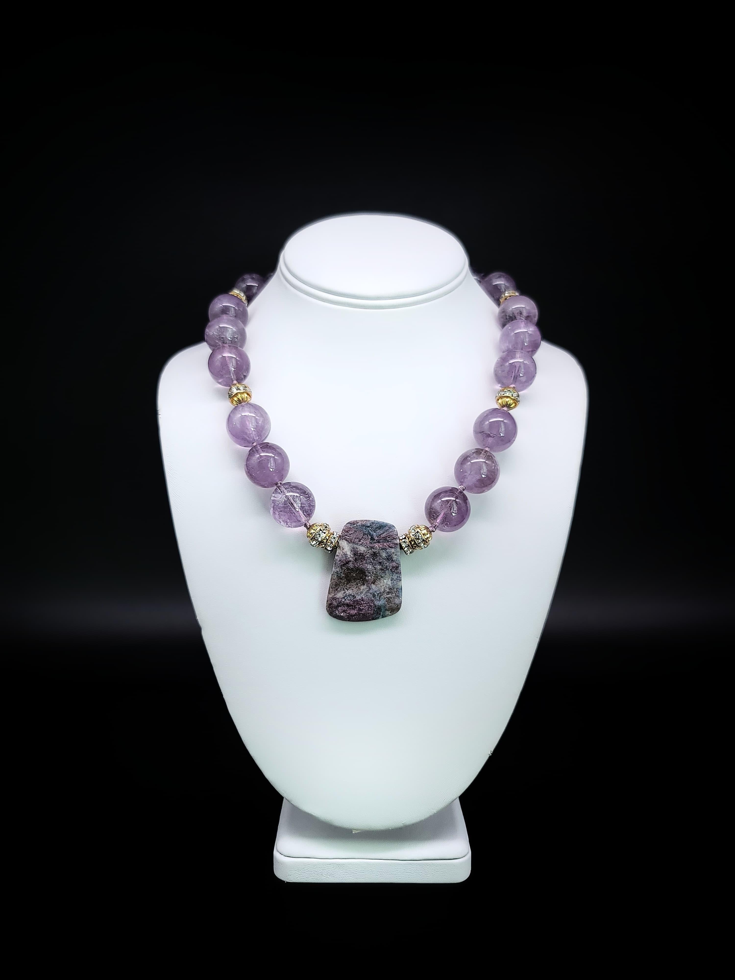 One-of-a-Kind

Paraiba Tourmaline presented in a two-sided rough-cut and polished plate serves as the centerpiece of this necklace strung of 20 mm. violet amethyst beads. 
Paraiba stone first discovered in Brazil in the 1980s is a highly valued, and