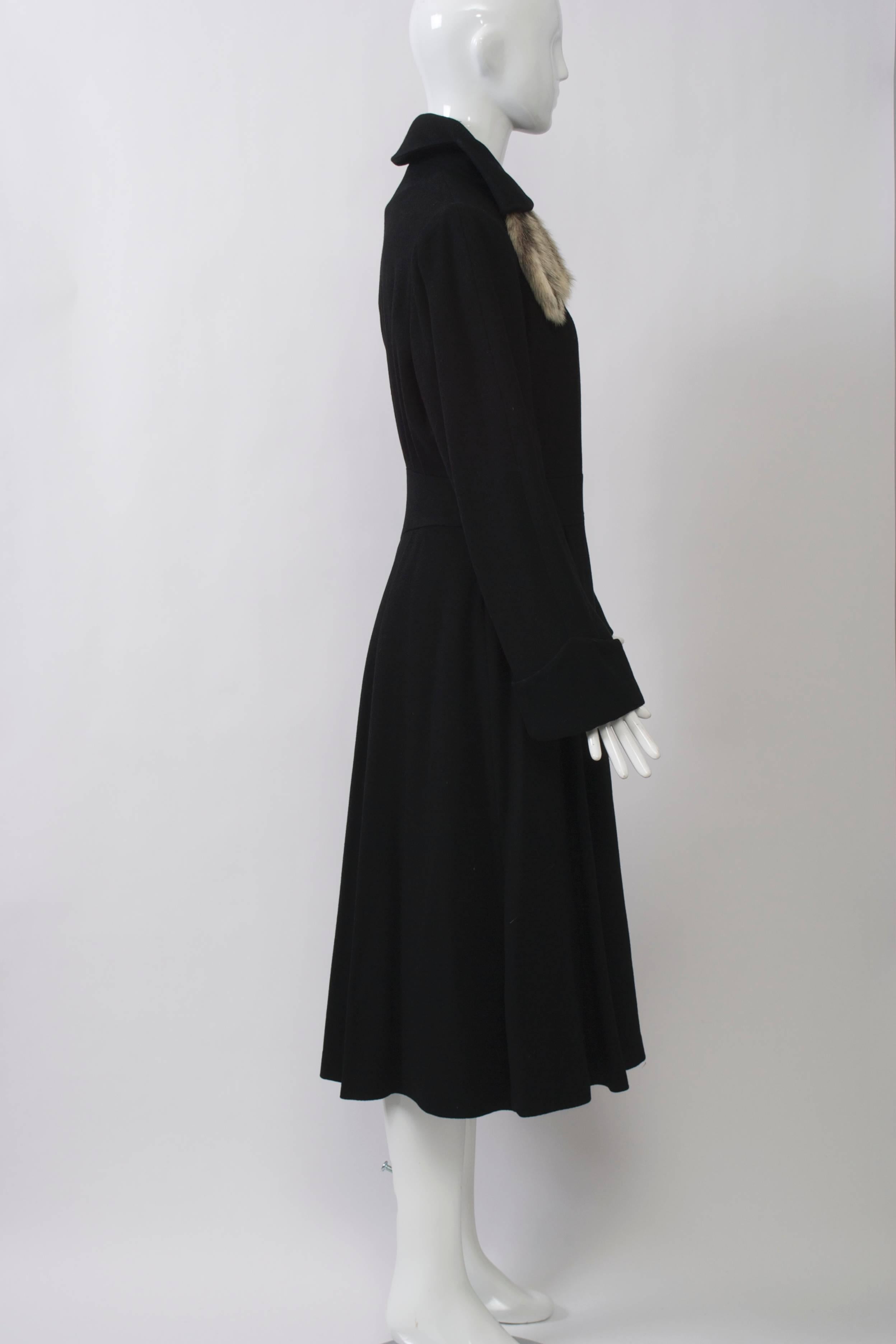 Wonderful detailing on this black wool coat featuring an inset waistband and high collar with fur tails. Other interesting details are the back pleats and pointed cuffs. Approximate size 6.