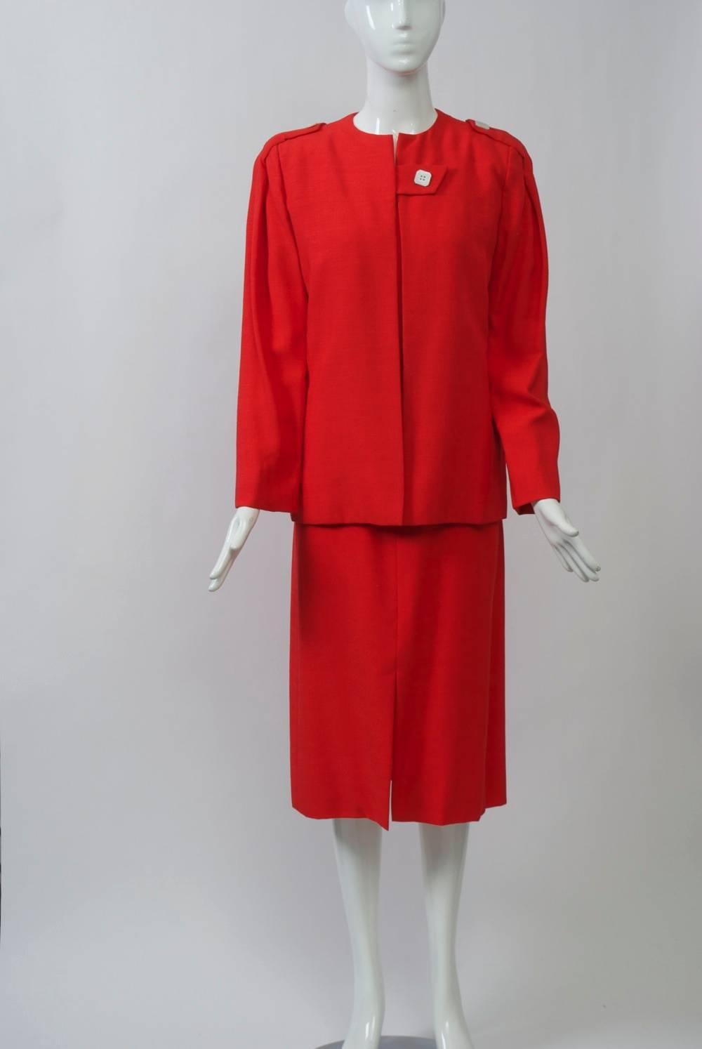 1980s Pauline Trigére dress and jacket in a red linen-blend fabric, the sleeveless sheath dress with square neckline, shoulder tab detail with pearl button closure, and side back zipper. A matching hip-length jacket features a similar tab closure