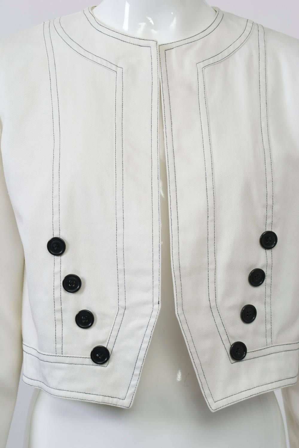 1980s white cotton cropped jacket by Oscar de la Renta features black topstitching at the edges and diagonally placed decorative black buttons from the bottom front corners towards the armhole. The slightly cut-in front edge is a nice detail. Padded