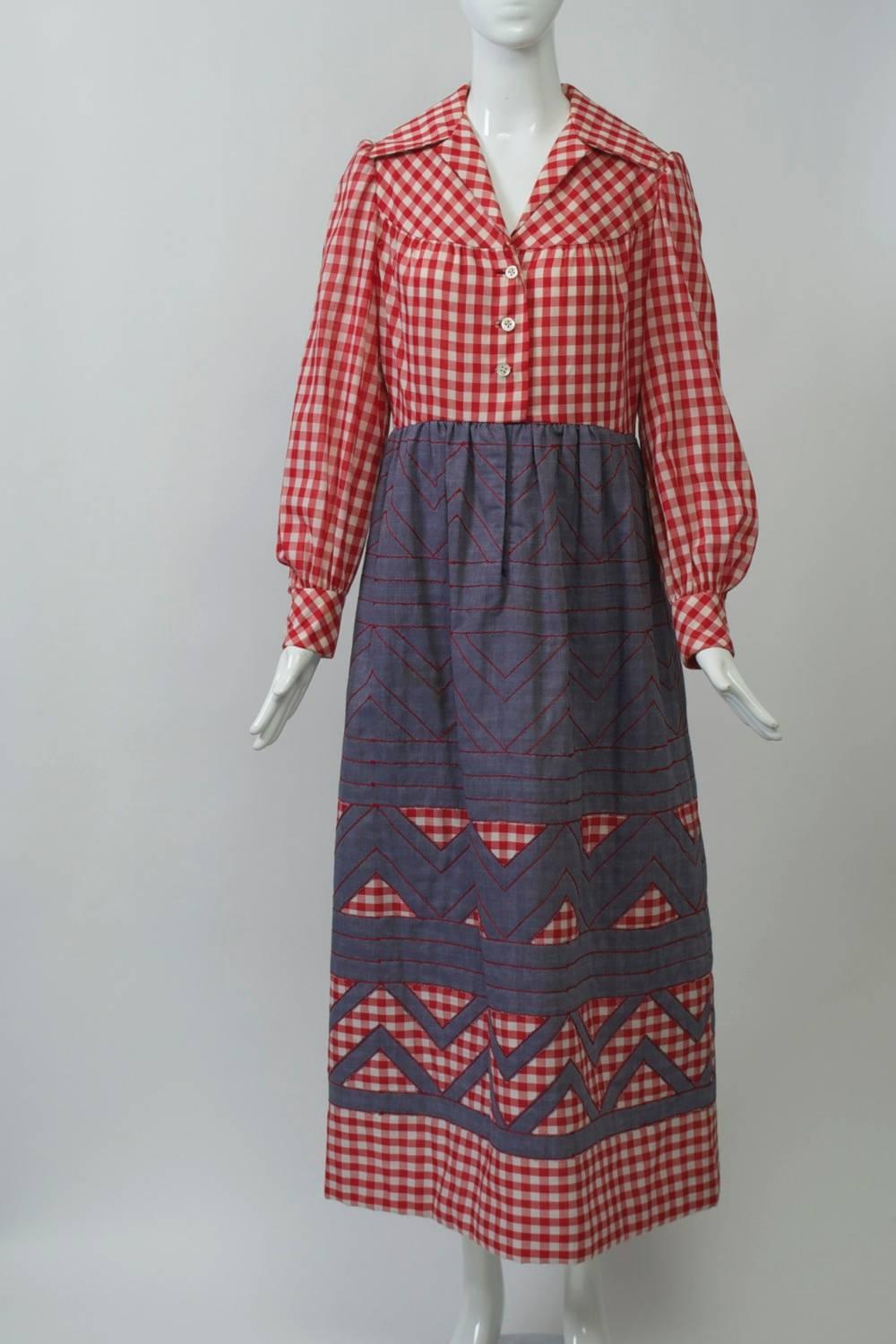 1970s maxi dress, its shirt-style, high-waisted bodice in red and white gingham checks with wide collar and yoke. Below is a denim-colored cotton skirt, its top half featuring red stitching in a banded and zigzag pattern, which is repeated as