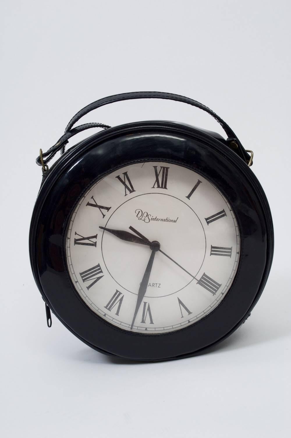 Black patent circular shoulder bag with roman-numeral clock face is a conversation piece. clock runs by battery and is housed in separate interior compartment. Top zipper.