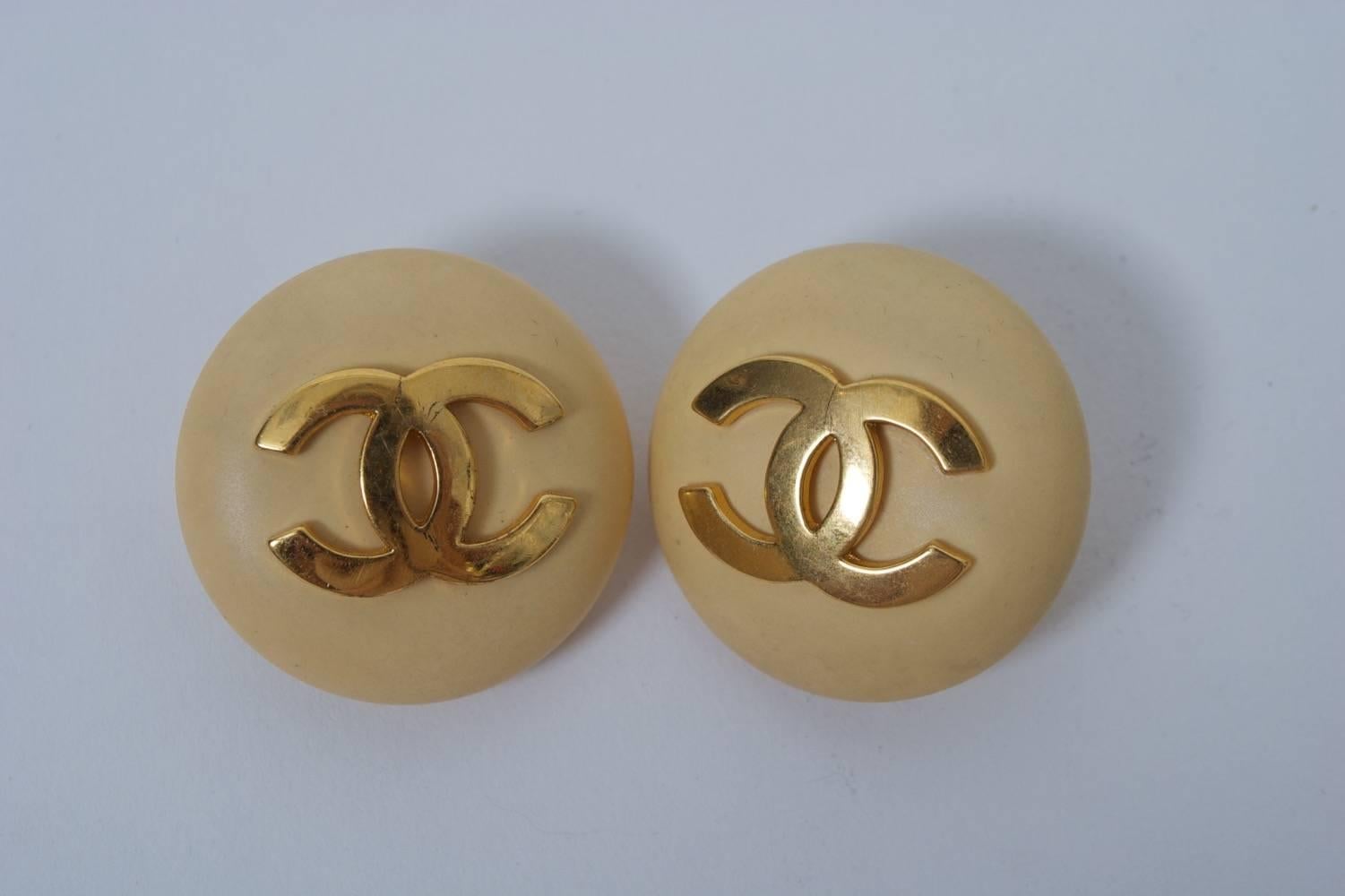 Classic Chanel button earrings in beige plastic or resin with double-C logo in gold metal. Clip backs with oval identity plaque dating design to 1987.
