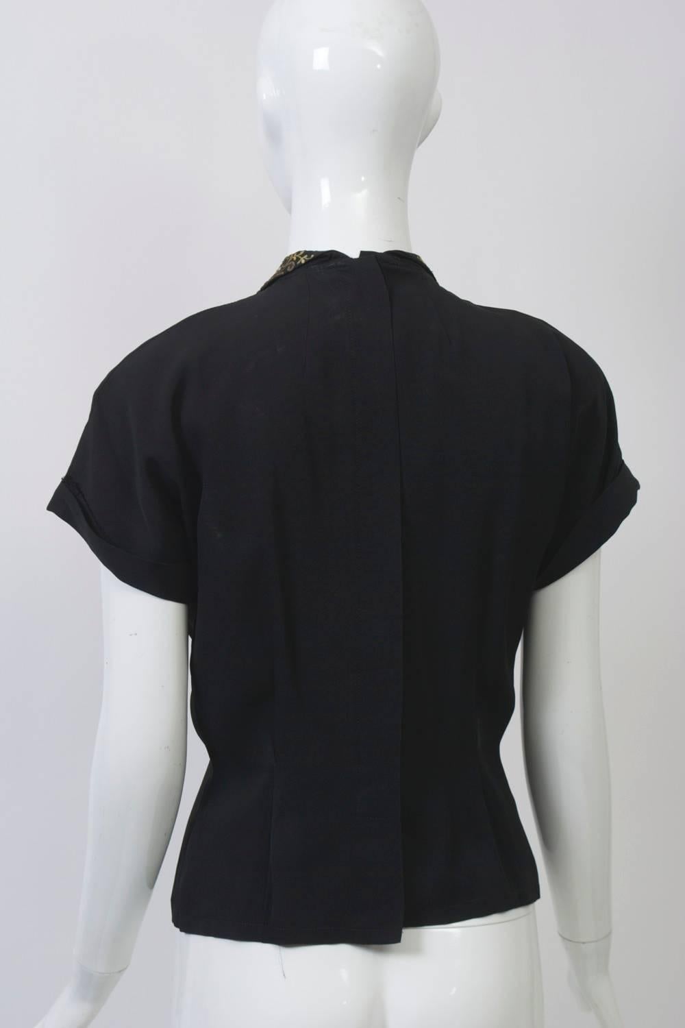 Charming black crepe blouse, late 1940s-early 1950s, featuring an embroidered and pearl-decorated collar, short sleeves with turned-back cuffs, and hidden buttons down the back. Double darts nip in the waist.  Size S-M.