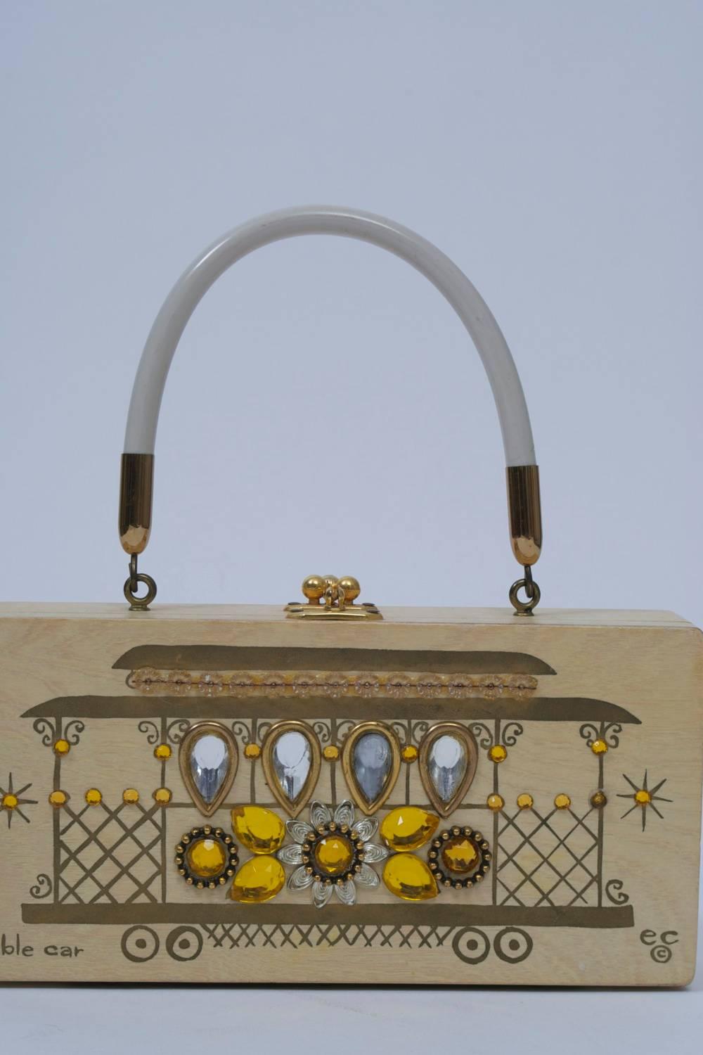 During the 1950s and '60s, Enid Collins produced a popular and collectible line of themed and decorated handbags, both totes and box bags. This wooden box bag celebrates the cable cars of San Francisco, featuring a light wood with gold painting and