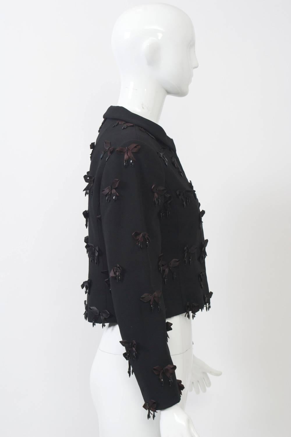 Early Bill Blass jacket in black wool embellished all over with satin and beaded bows features a small collar, bound buttonholes with satin buttons, and is shape at the waist. Fully lined.