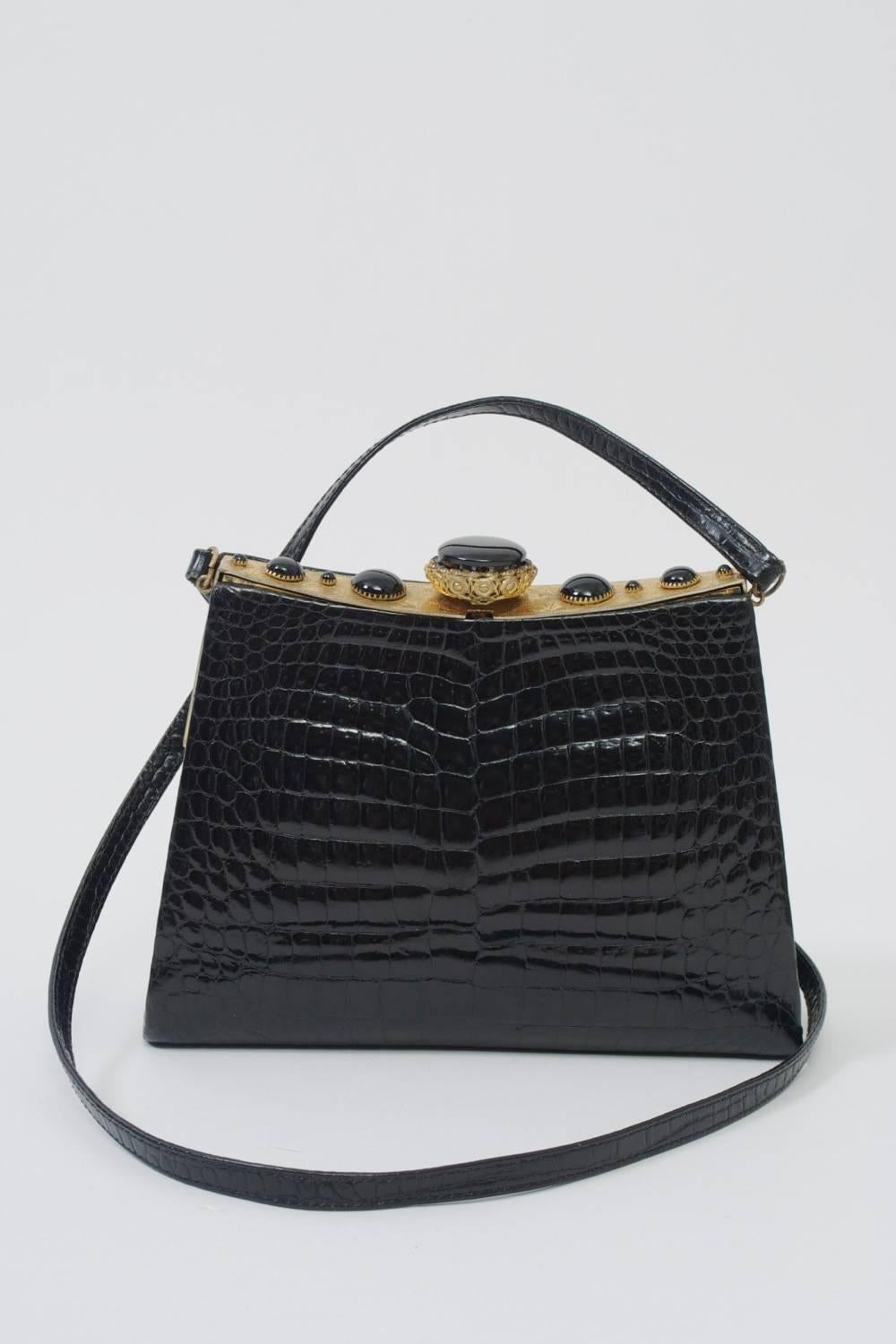 Shoulder bag of black crocodile featuring an incised  gold metal frame decorated with graduated black cabochons centering a larger one in a filigree mounting. Narrow croc shoulder strap. Black leather interior with zippered  compartment.