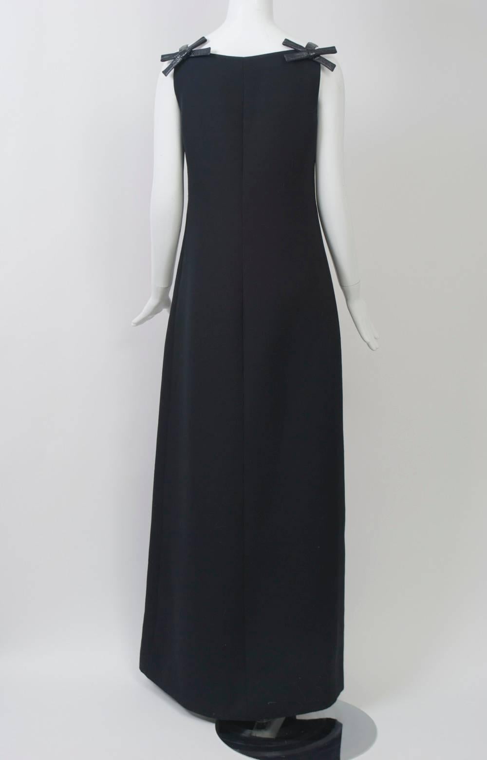 André Courrèges maxi dress, c.1970, in black polyester with square neckline and narrow shoulder straps in black patent leather terminating in bows front and back. Simple, body skimming shape with A-line skirt. Side zipper. Lined. Labeled size 