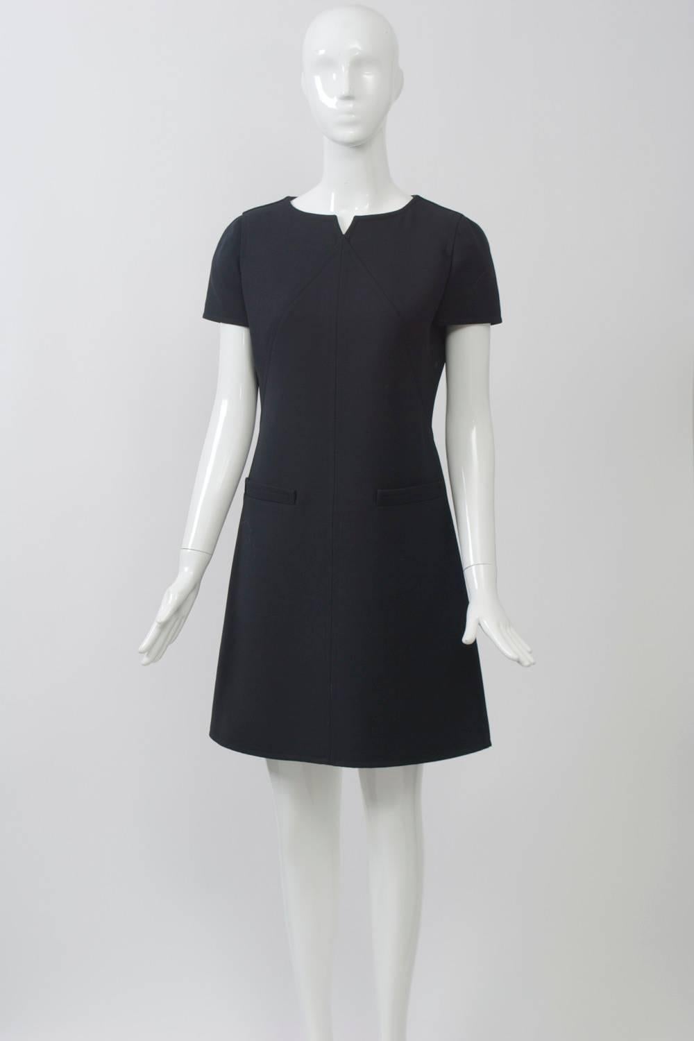 Perfect little black dress in wool from André Courrèges features welted diagonal seaming that forms an inverted V on the bodice, resulting in a notched-v at the center of the round neckline. Other features include faux pockets at the hips and a