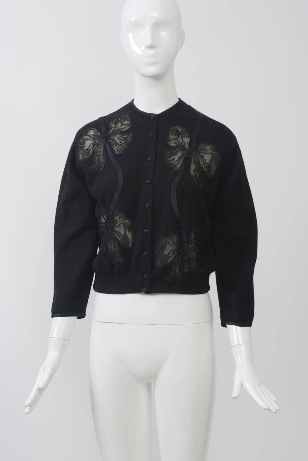 Some of the best vintage pieces from the 1950s-'60s are the decorated cardigans. This example, in black cashmere, has large illusion bow cutouts connected by ribbon on front and a single bow at the left back. The short cardigan has black satin