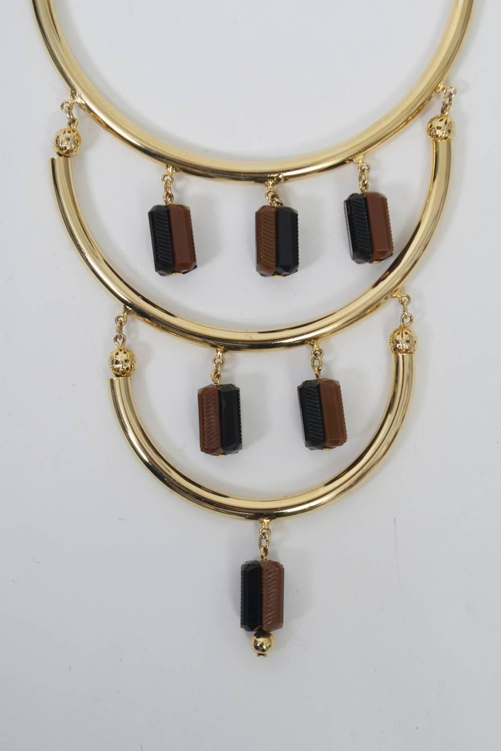 Tiered goldtone necklace by Hobé consisting of graduated half-circle tubes, the top through which the chain passes. Each tube suspends squared beads, half black, half brown. Signed oval plaque near clasp.