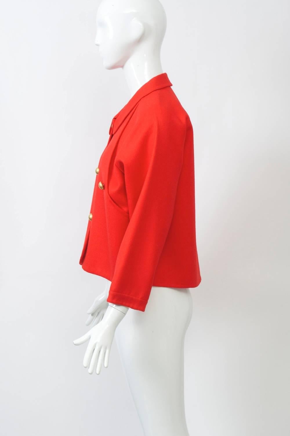 Geoffrey Beene c.1980s double-sided wool jacket in orangey red featuring over panels in front shaped around armholes. Loose fitting, boxy shape with raglan sleeves, small collar, and matte gold buttons at front and closing panels/pockets.