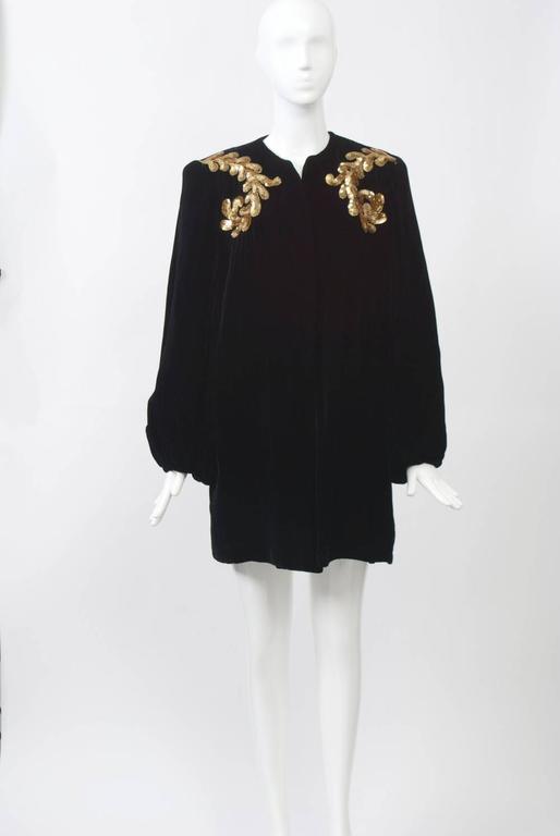Black velvet three-quarter coat in black velvet embellished with gold sequined leaf design curving from the shoulder to the armhole. Collarless, with balloon sleeves and white quilted lining for warmth. Square shoulder with pads. Approximate size