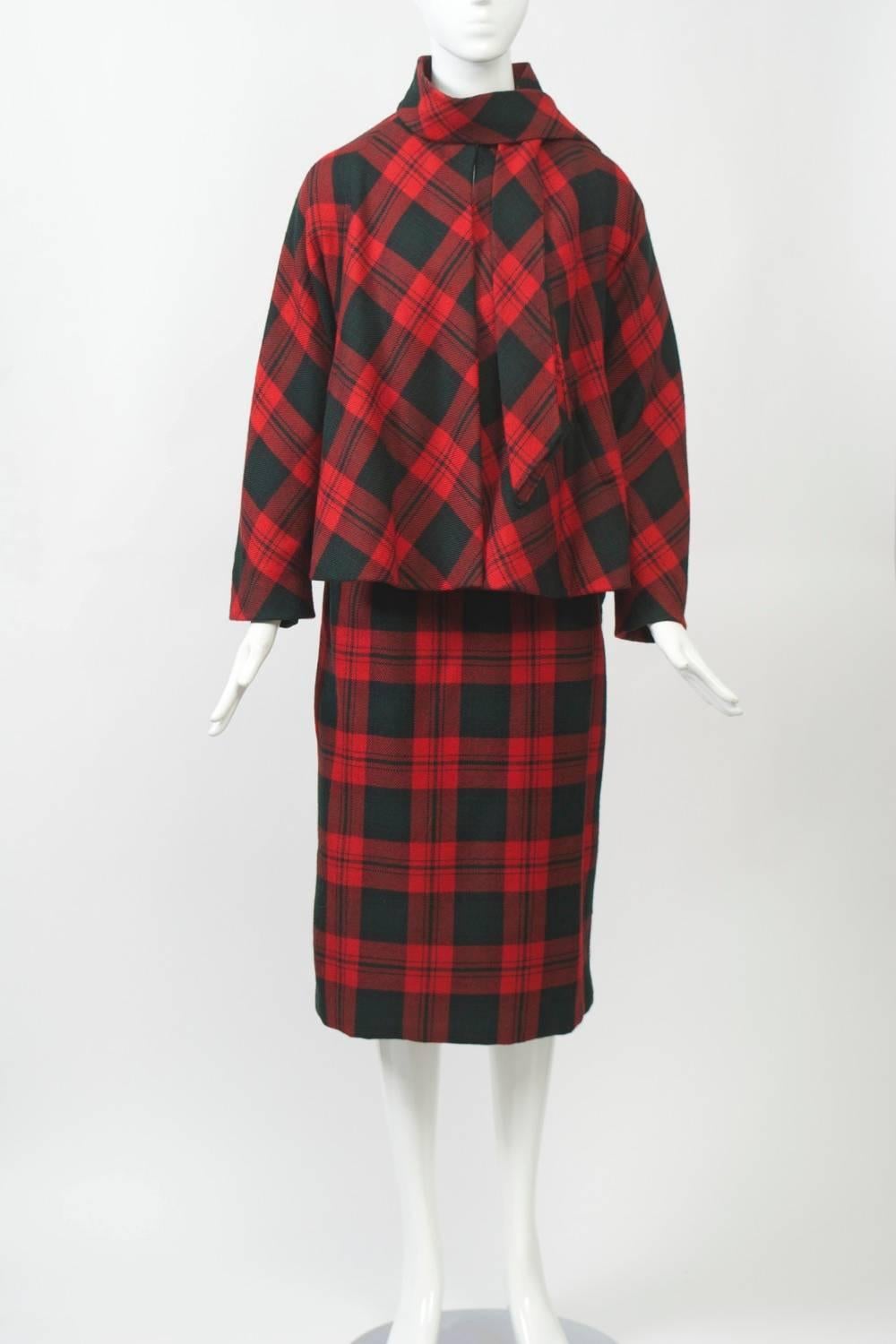 Vintage Pauline Trigere suit in red plaid wool dated 1962. The swing-style jacket has dolman sleeves and a tie collar and tops a slim skirt. Underneath is a dark green knit surplice top, which matches the lining of the jacket. Taped label from Saks