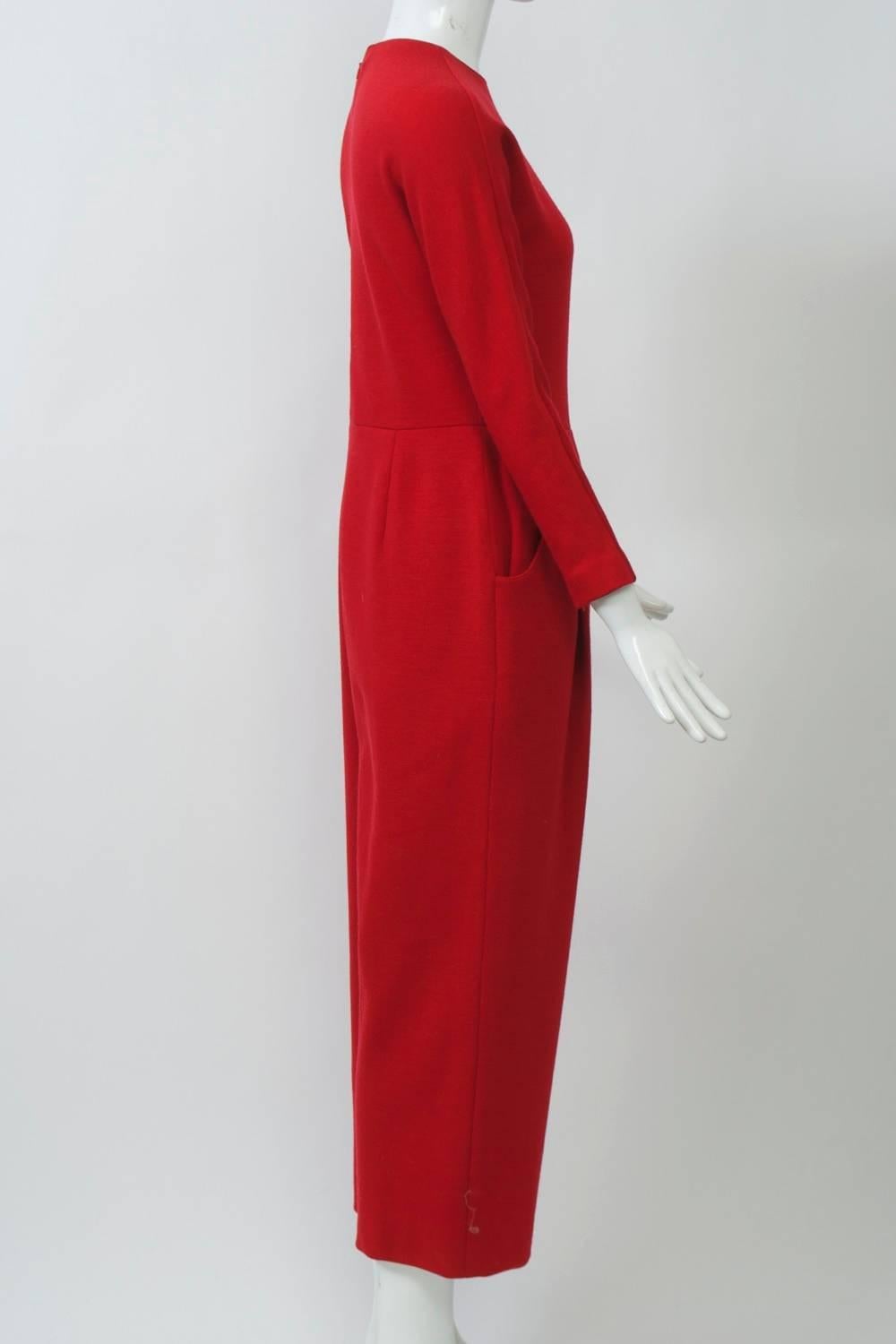 Jumpsuit by Geoffrey Beene in red wool knit featuring a round collar, waist seam with faux fly front, dolman sleeves with zippered wrists, and curved side pockets. Ankle-length pants. Back zipper; bottom lined. Approximate contemporary size 6.