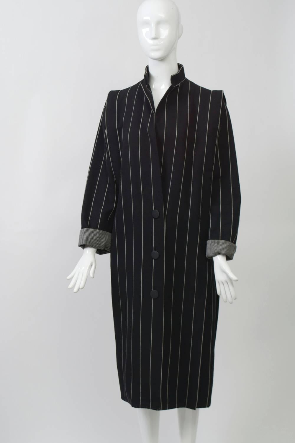 Pencil-striped coat in double-faced black and white worsted wool. Loose cut with stitched flange around shoulder line, three-button low closures, and turned-back cuffs. Slit pockets hidden in flange. Lightweight. Approximate size M.