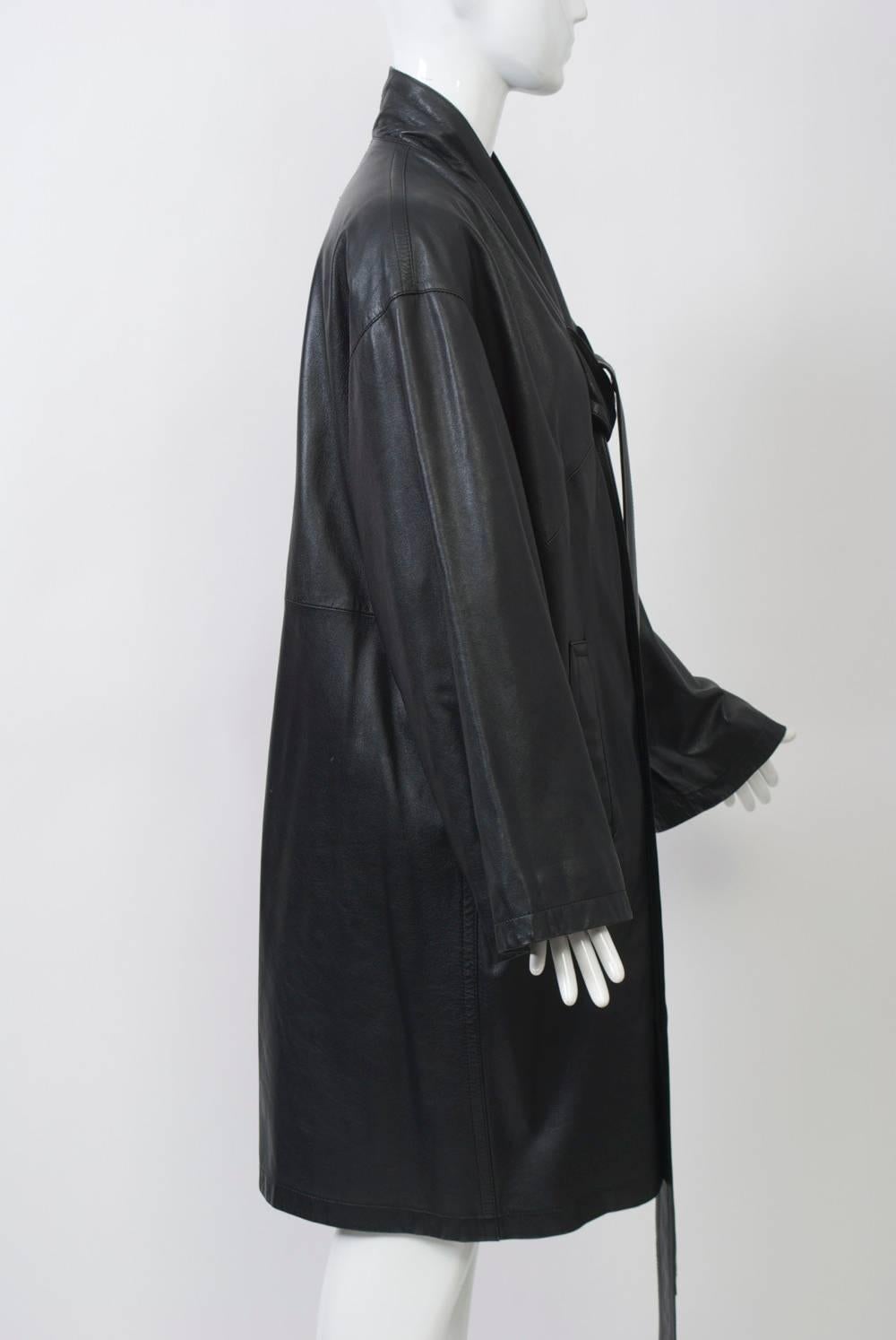 Kimono-style black leather coat by Jean Paul Gaulthier with dropped shoulders and wide sleeves. The collar band leads to two long ties to knot in front. Side pockets. Length is just above knees. 