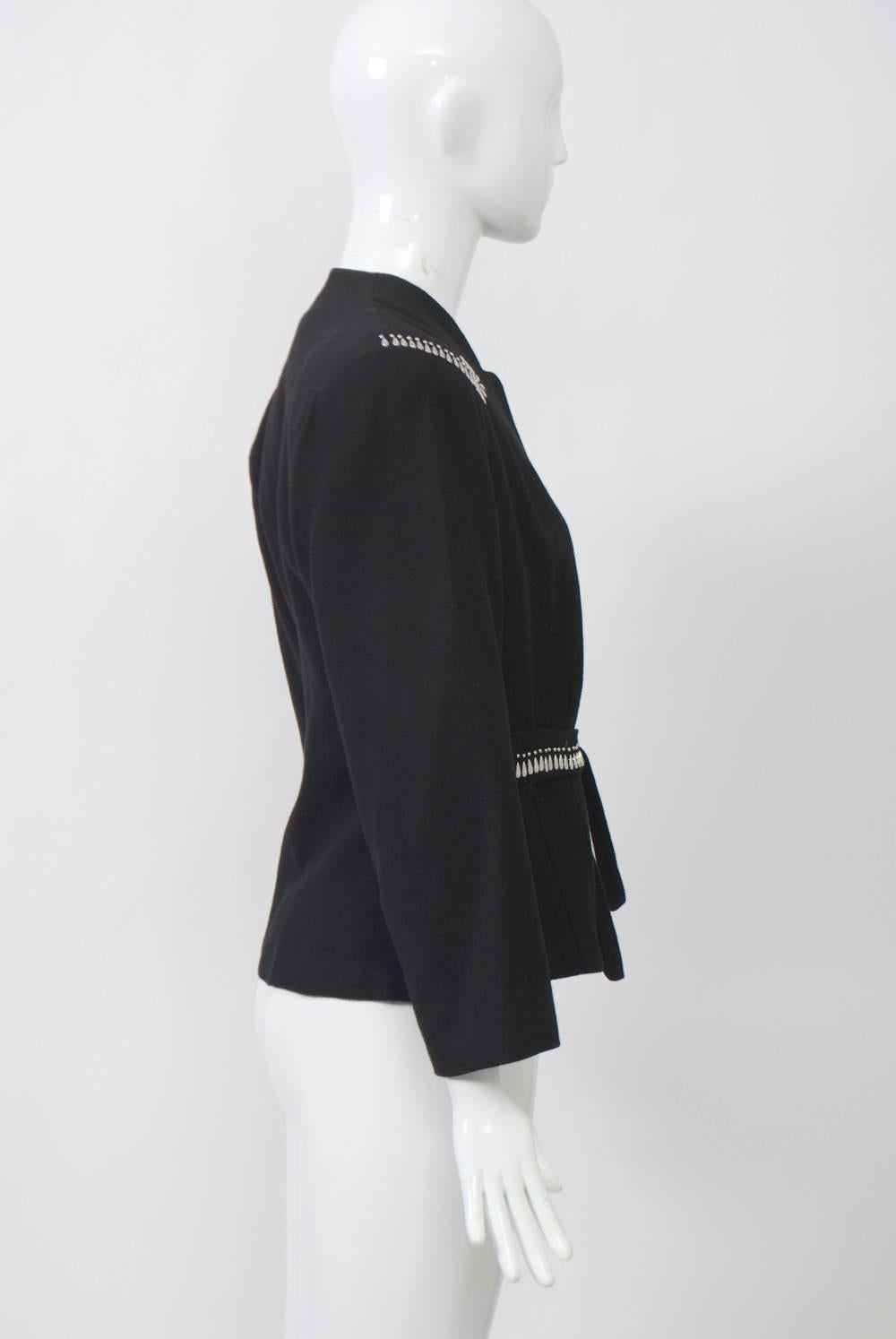 Black wool 1940s jacket with teardrop-shaped silver stud embellishment near shoulders and along front of self-tie waistband. Indented round neckline, square shoulders with pads, shaped body. Lined in black crepe.