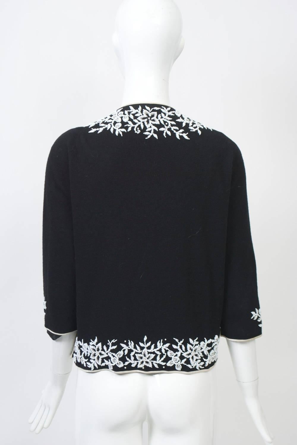 Black wool knit cardigan with white foliate beading around borders and decorating the three-quarter length sleeves. Edges bound in white satin, as are side slits, which can be hooked closed. Lined.