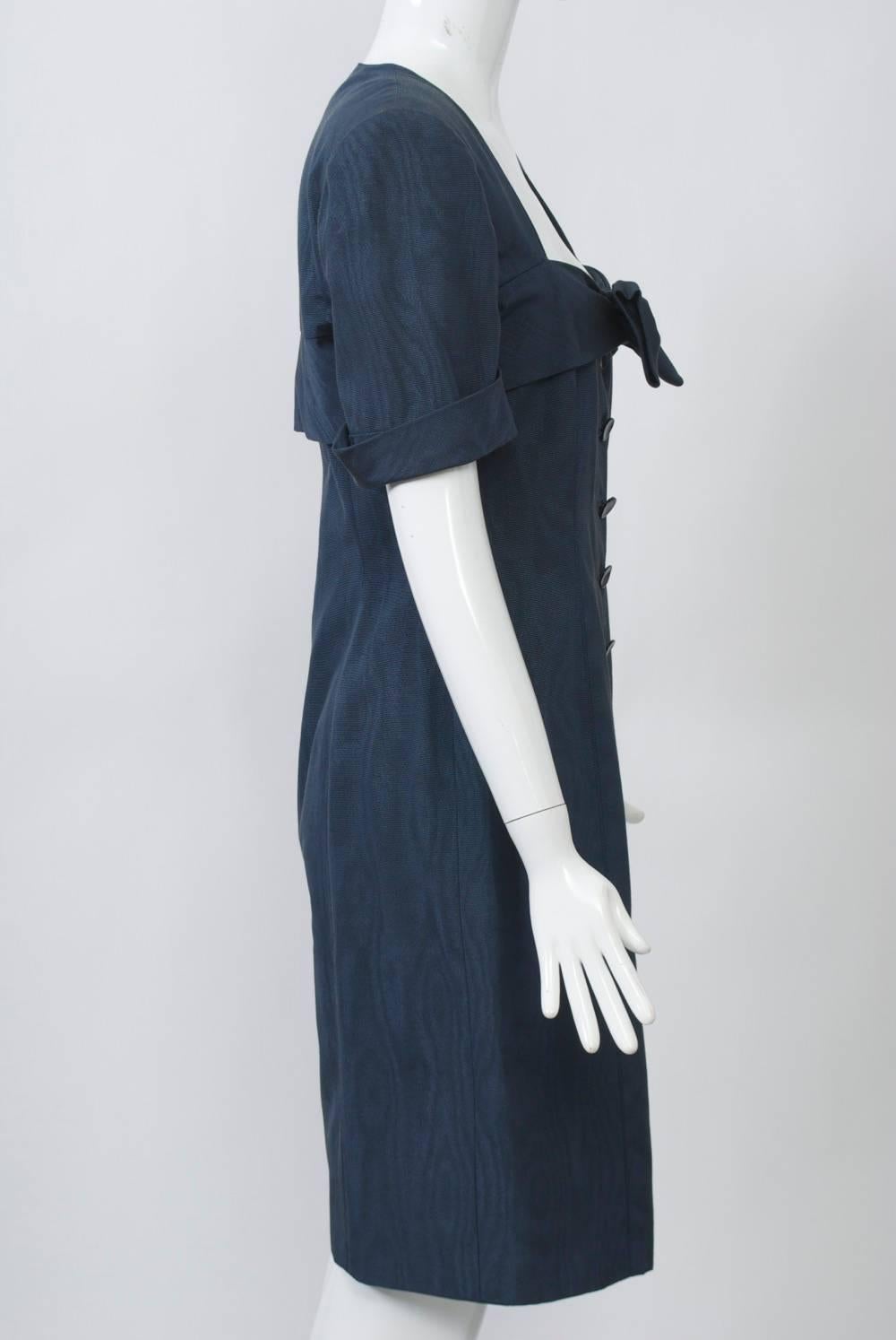 Steel blue moiré dress by Ungaro featuring a low square neckline with large bow attached to a wide overlaid band that circles the dress across the bust and back. Buttons down the front. Short sleeves with turned-back cuffs and squared shoulders with