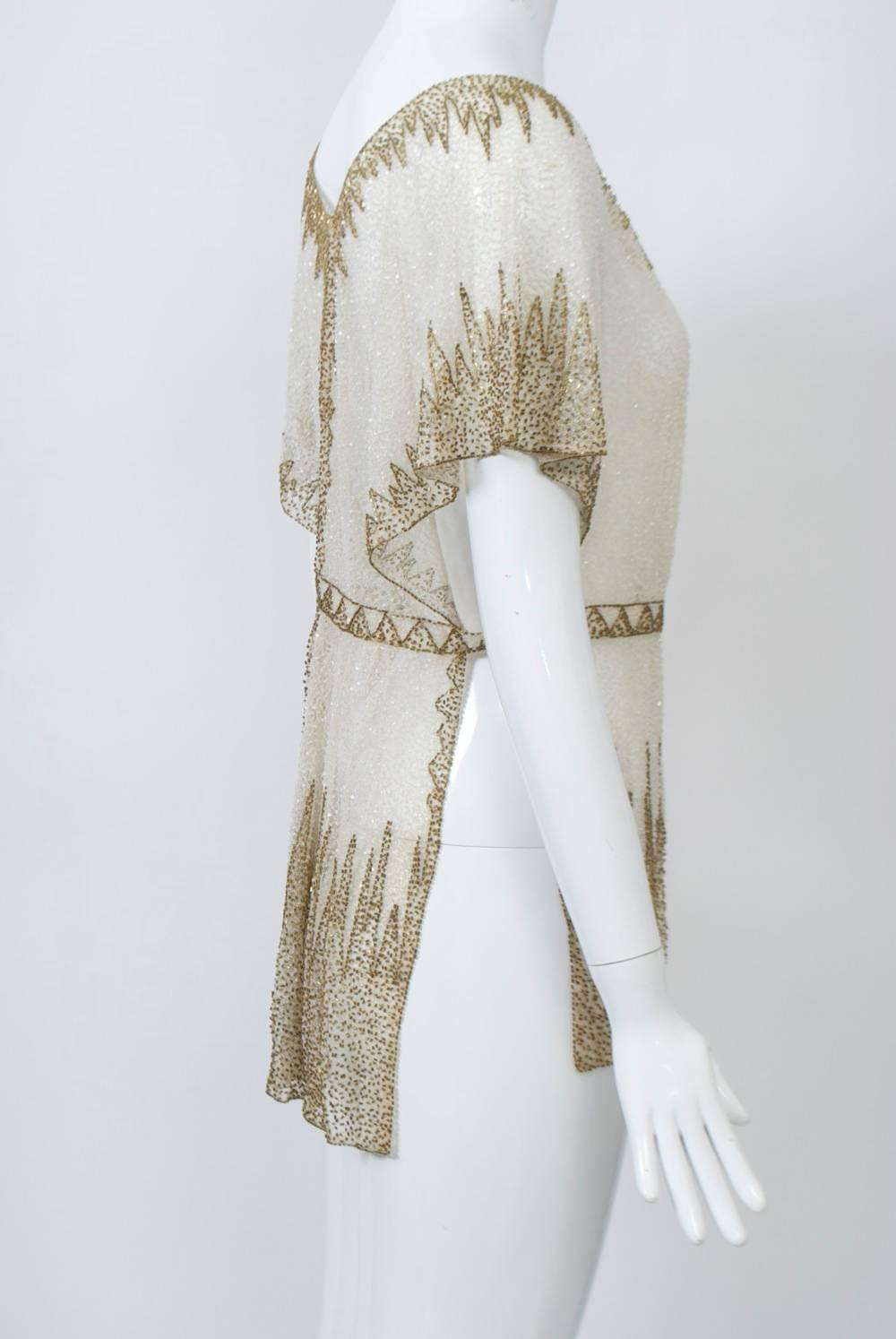 Extravagantly beaded sheer tunic of tiny crystal beads overlayed with a deep flame-pattern border at the hem in gold beads, a pattern which is echoed around the soft V-neckline and wide cap sleeves. Around the waist and across the open sides is a