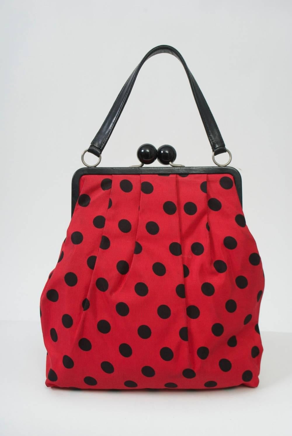 Fun Moschino handbag in red taffeta with black polka dots with several pleats in the fabric under the black leather frame. Single handle of black leather. Shiny black kiss clasp. Zippered compartment on interior with silver metal heart stamped