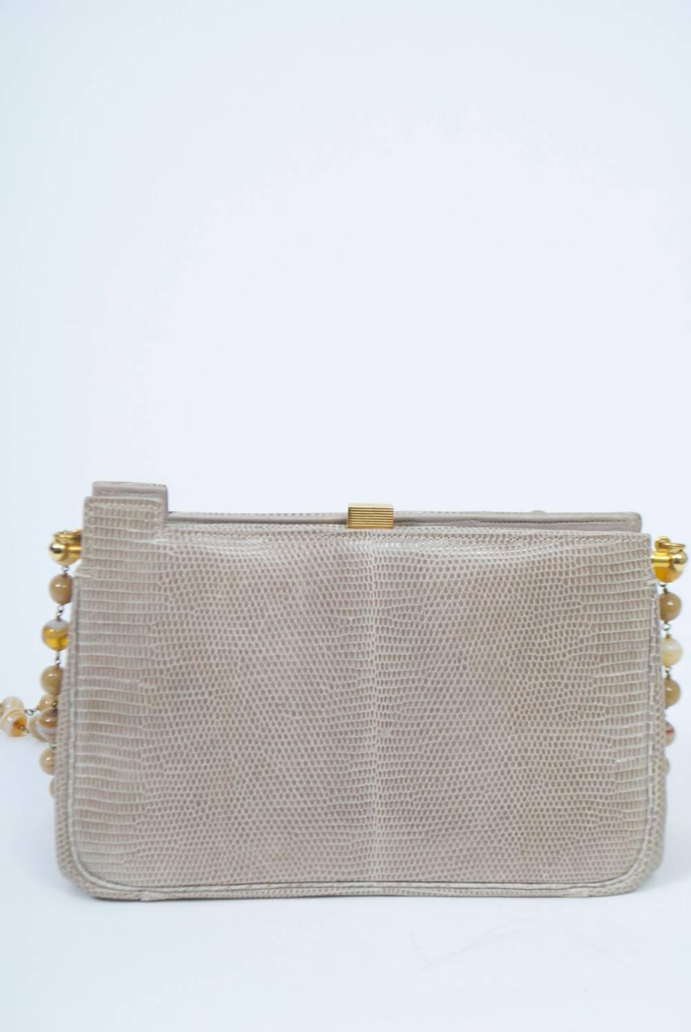Love this bag! Meticulously crafted of taupe lizard, the structured handbag features a shoulder strap of complementary beads accented by dangling rhinestone-studded wood beads, which motif also embellishes a front corner of the body. Closed