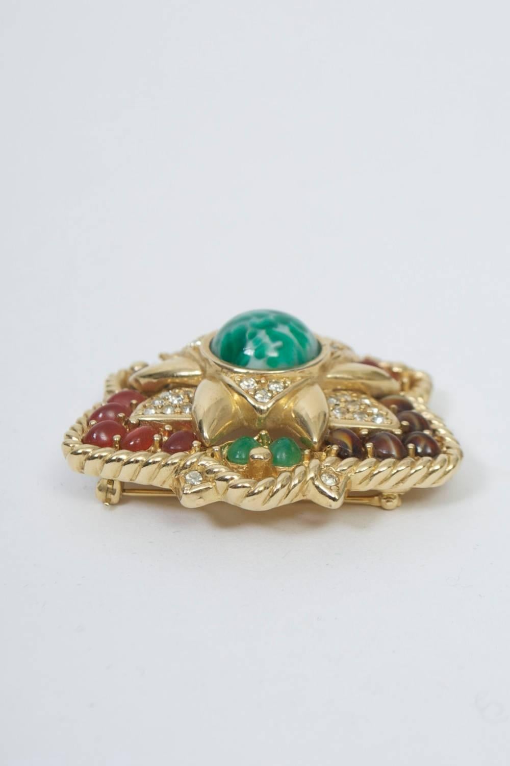 Ciner brooch of gold tone metal set with mutilcolored stones. Basically triangular in shape with protrusions that lend it a star pattern, each of the main three sections set with smooth stones in green, red, brown, respectively, within the rope