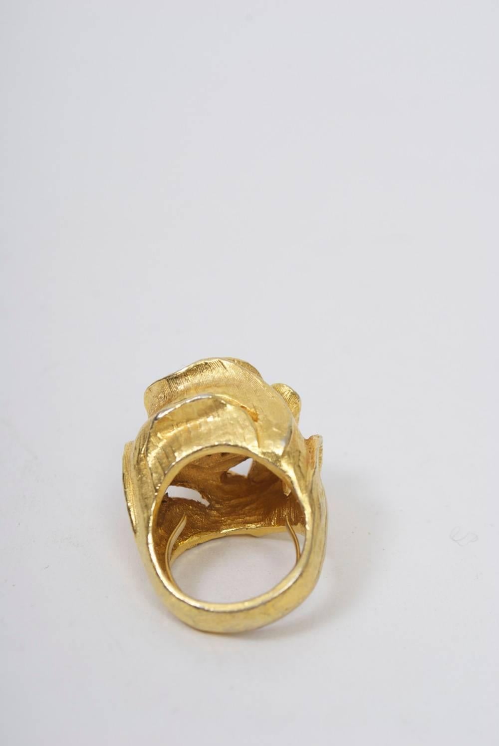 Heavy gold metal ring of floral shape centering a round turquoise stone. Gold metal is nicely textured and has an interior adjustable finger hold. Known for her chunky jewelry, Rader was active mostly in the 1960s and '70s; her production was