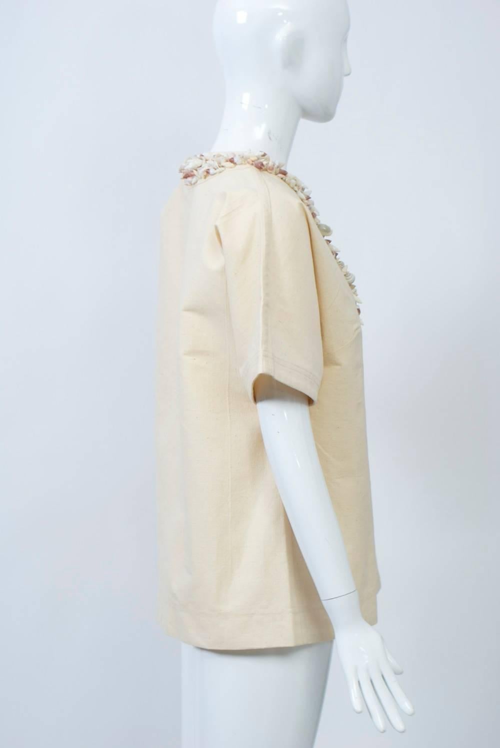 A unique vintage tunic of beige canvas thickly embellished with complementary small shells around the slit neckline. Short, raglan sleeves. Slips over the head. 