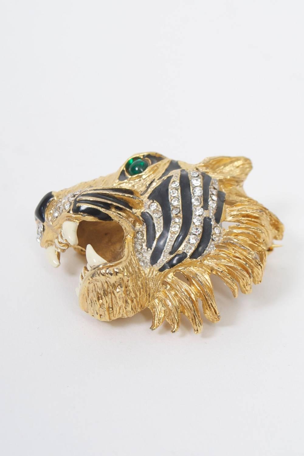 Roaring tiger head brooch by Butler & Wilson, 1980s, based on a Hattie Carnegie original. Composed of grooved gold metal with black enamel and rhinestone stripes, ivory enamel teeth, and a green stone eye. Unsigned, but rectangular stamp with A