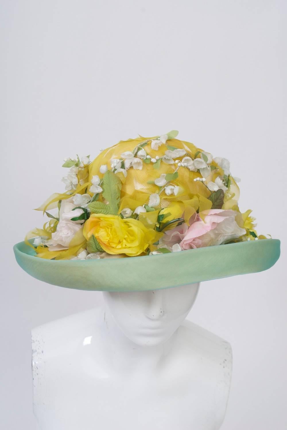 Profusely embellished natural fine straw hat with wide brim trimmed in pale green organza, the crown covered with ribbons of yellow organza, and the upper side of the brim decorated in pale pink and yellow flowers accented with lily of the valley.