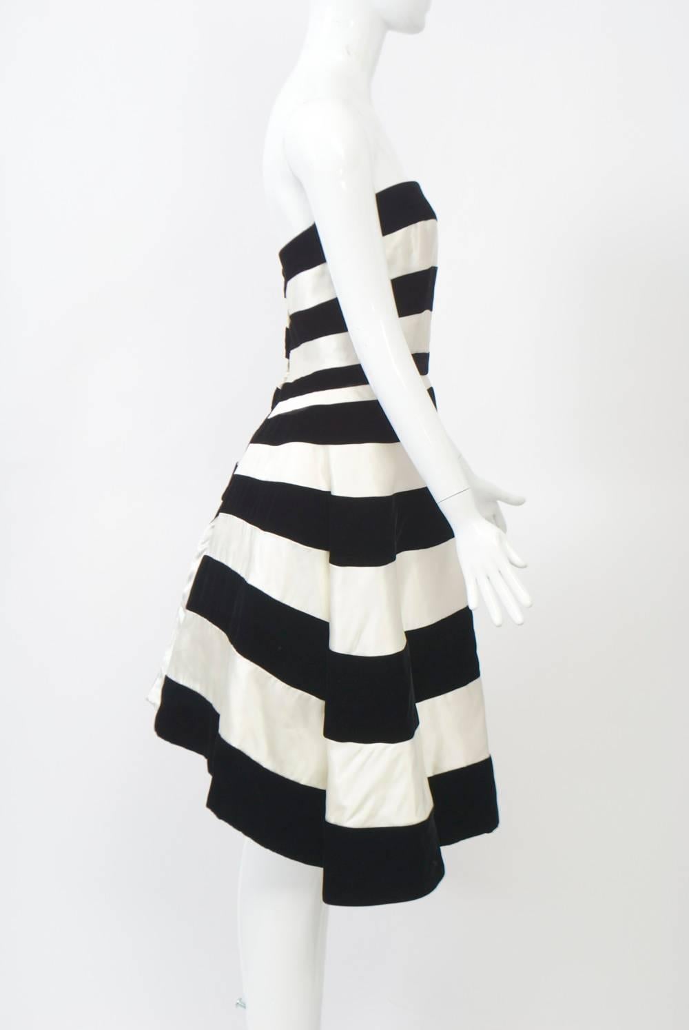 One of Victor Costa's best designs, this strapless cocktail/evening dress is fashioned of white satin and black velvet alternating horizontal stripes with fitted bodice leading to an A-line below-knee skirt. The most interesting feature of the dress