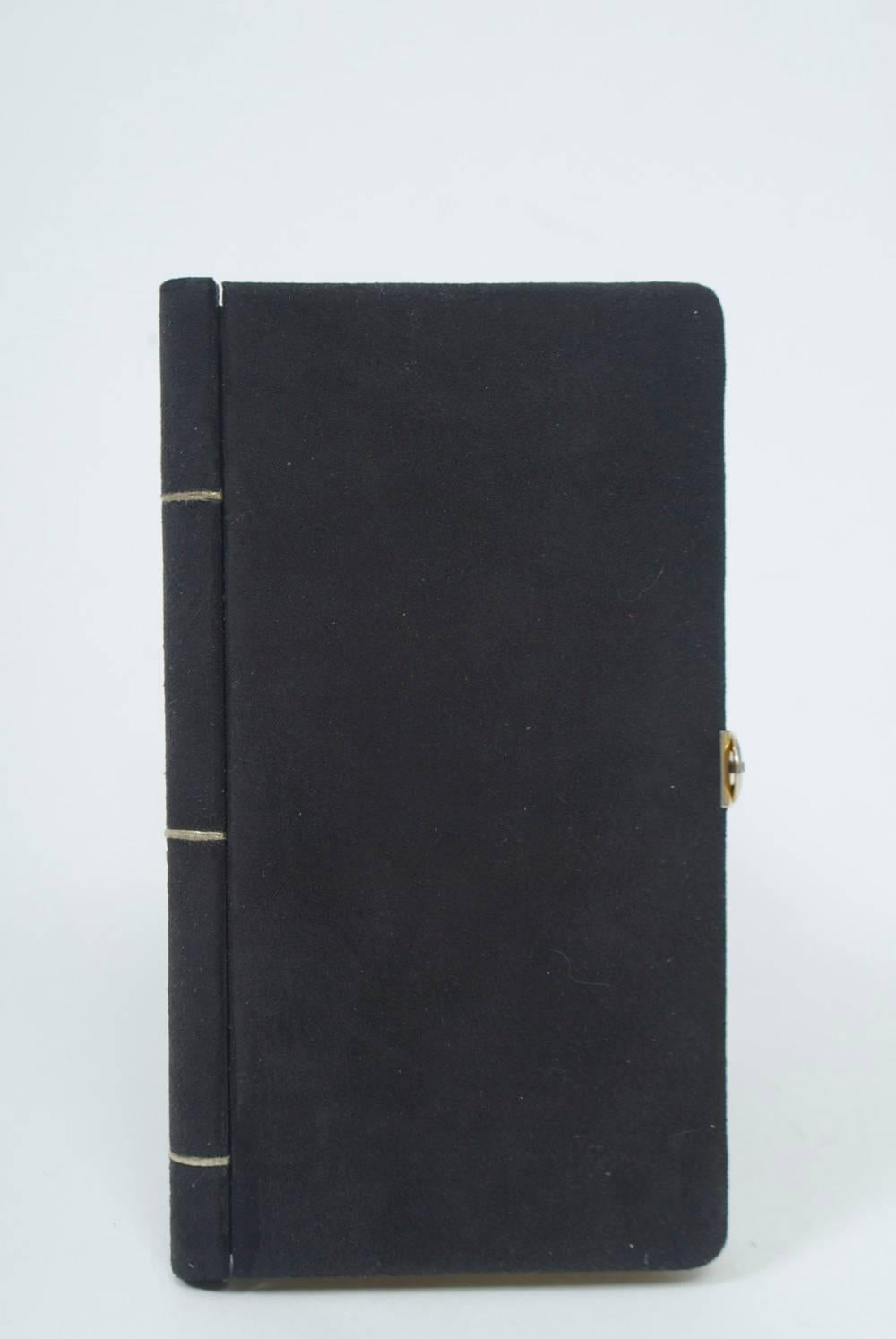 Unique black suede clutch in the surrealist mode, resembling a slim book and accented with three gold leather stripes on the binding and gold metal for the page edges, with a simple gold metal loop clasp. Fitted interior with multiple compartments