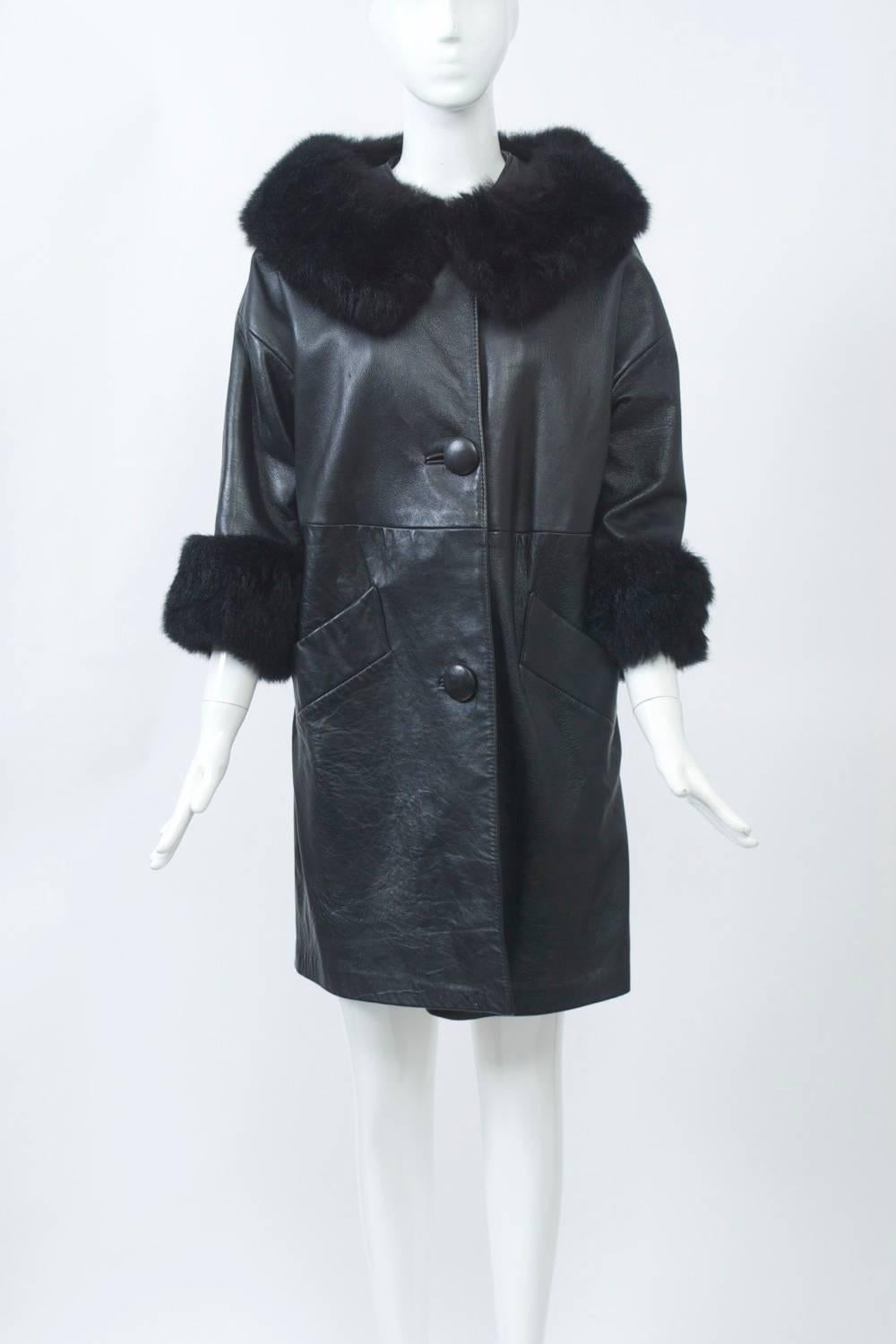 1960s short black leather coat with dyed opossum collar and cuffs. Straight cut, seamed around waist, with dropped shoulders and three-quarter sleeves. Slanted pockets and 3 large leather buttons. Red satin lining.