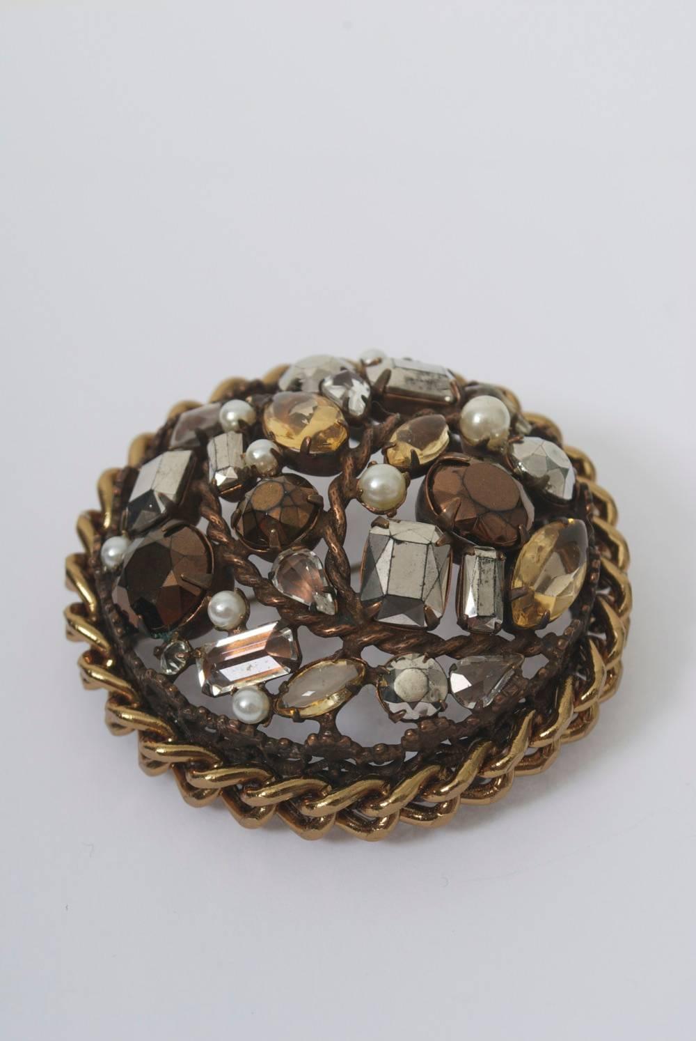 Circular brooch by Schreiner with openwork frame and chain circumference in dark bronze-colored metal set with various colored and shaped crystals and pearls. Concave shape lends the brooch three dimensionality. Marked 