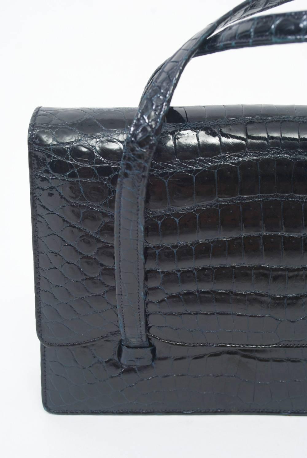 Small 1960s crocodile handbag from Artbag on Madison Avenue, NY, features an envelope style top with snap closure and double handles that attach below the flap. Black leather interior with zippered pocket on one side and open pocket with mirror on